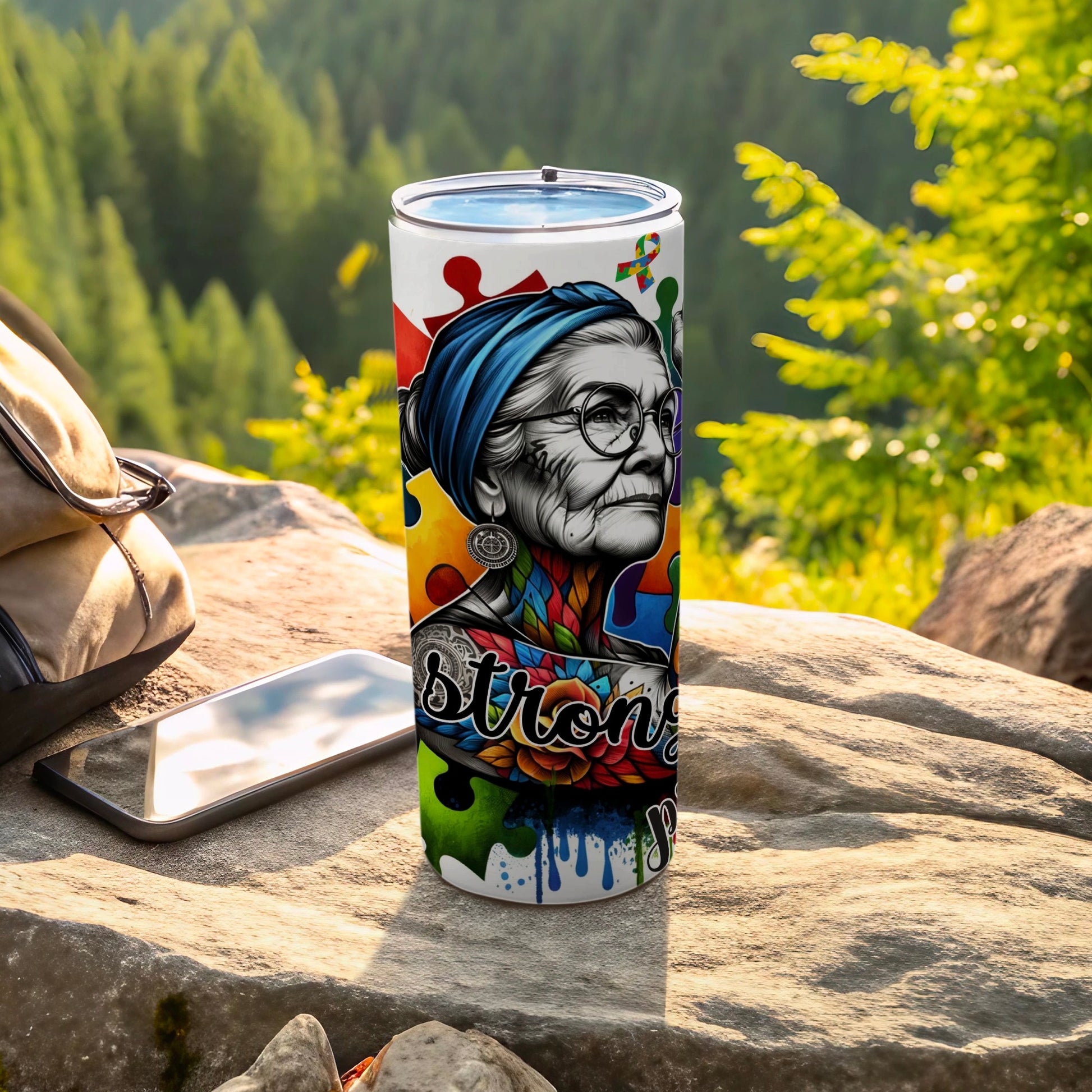Tumbler featuring a colorful portrait of an elderly woman wearing a blue headscarf, puzzle pieces, and the word "strong".
