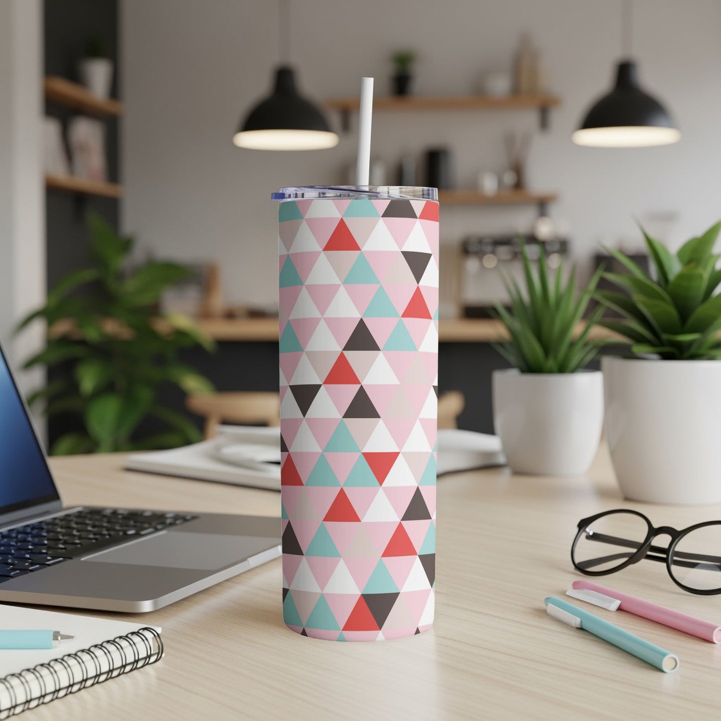Tumbler with abstract triangle pattern in pink, blue, and red on a desk.