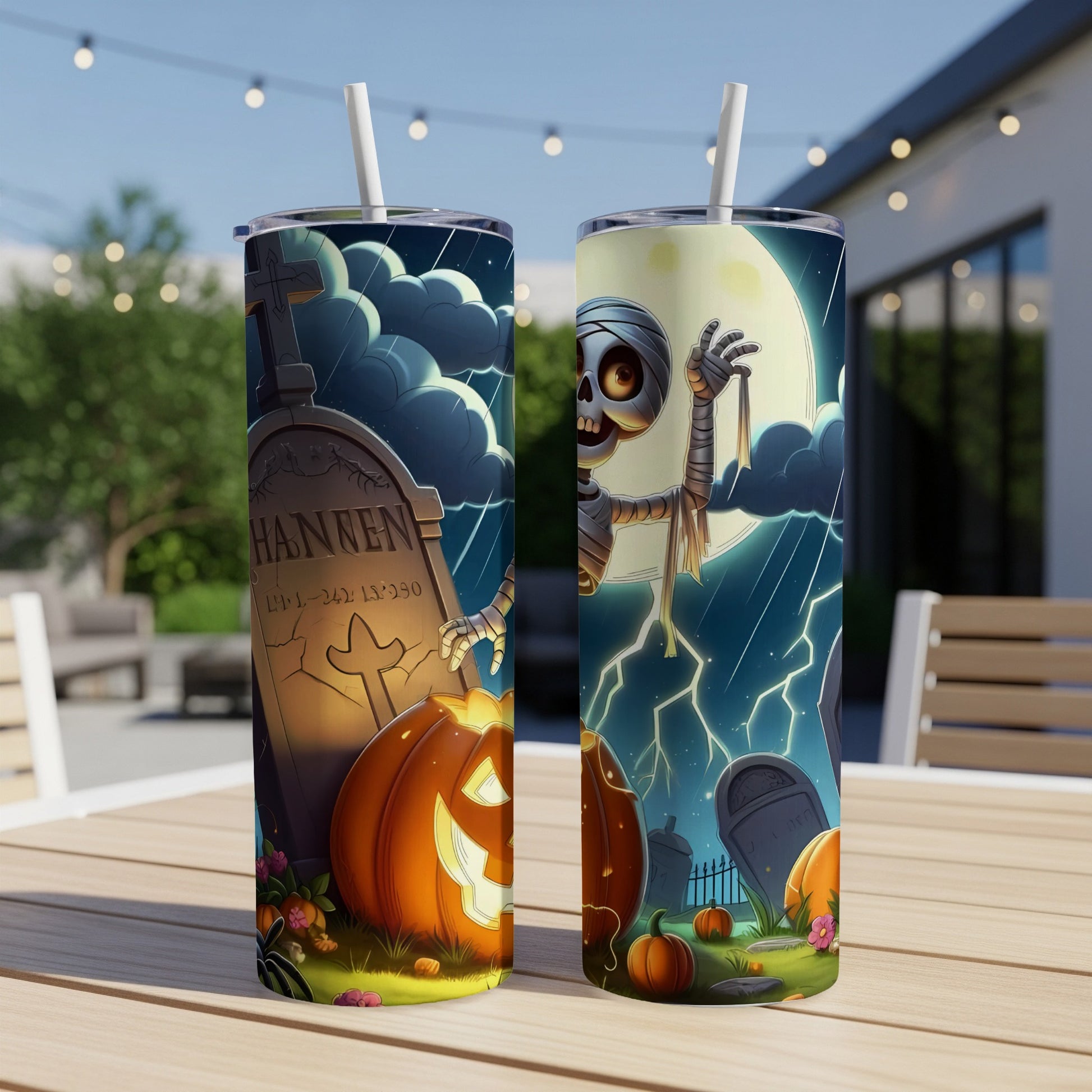 Two Halloween tumblers with graveyard and mummy designs on a picnic table.