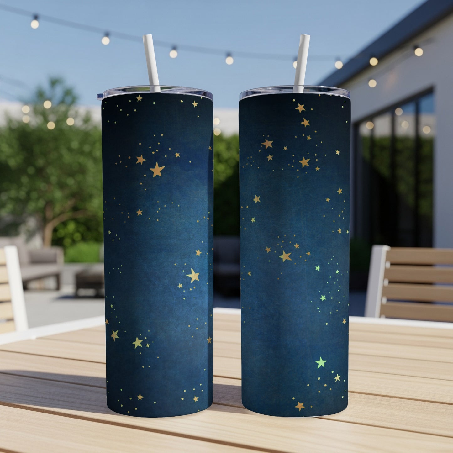 Two dark blue tumblers with gold star patterns and white straws, displayed on a wooden table.