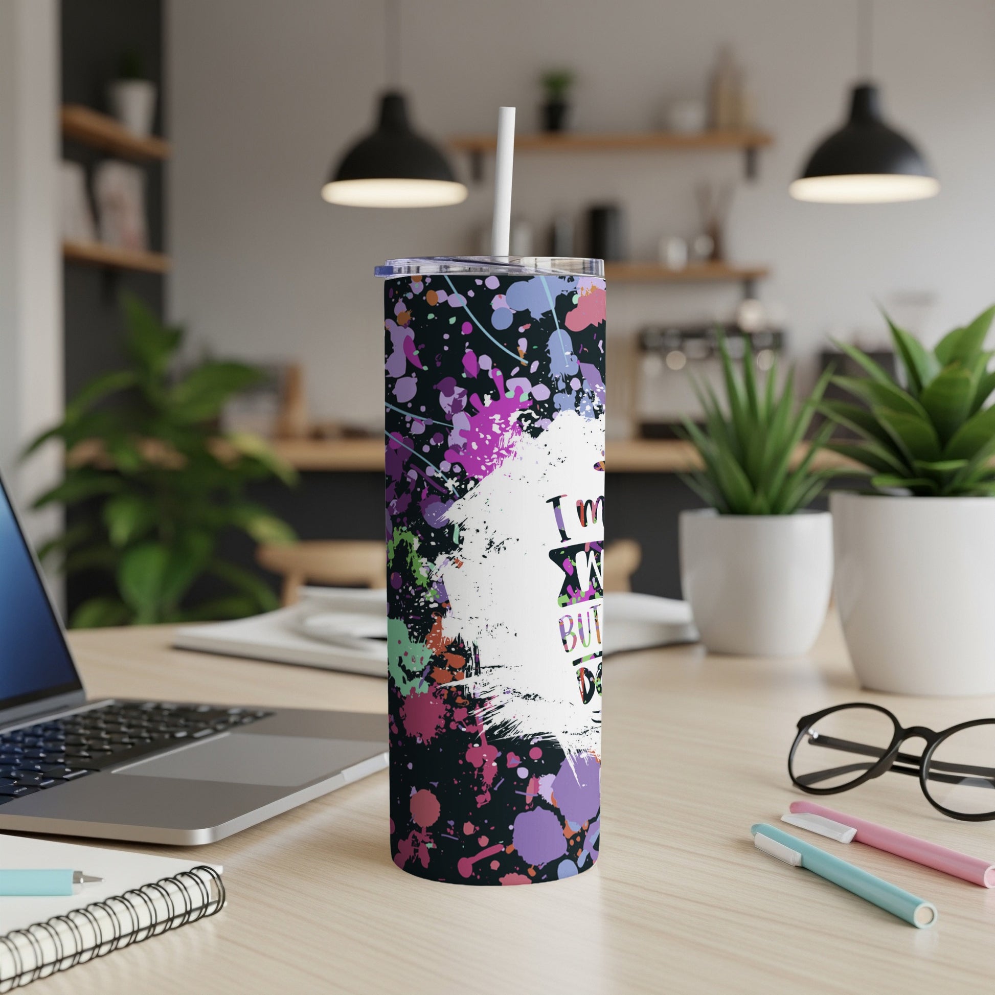 Abstract paint splatter tumbler with a straw on a desk.