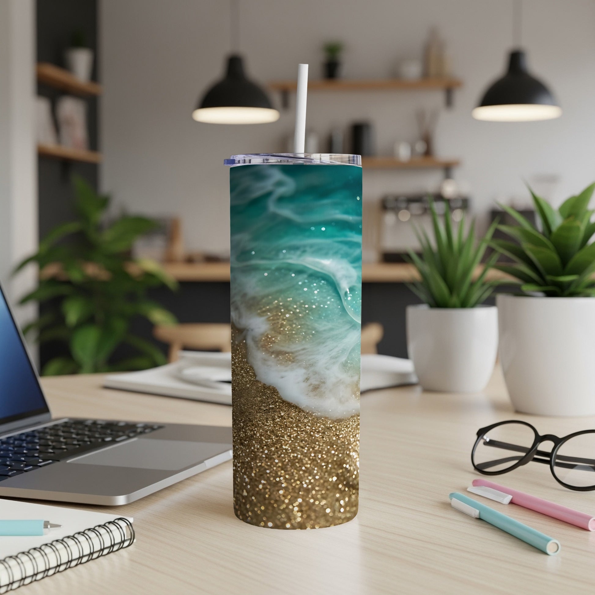 Glittery gold and turquoise ocean wave tumbler with straw on desk.