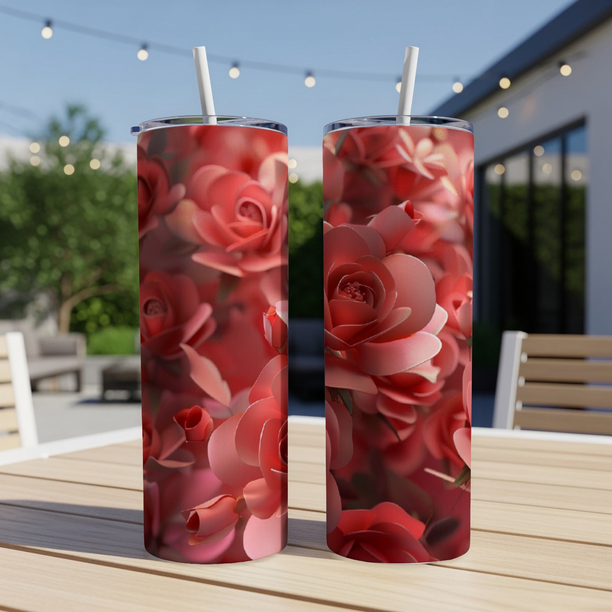 Two pink rose pattern tumblers on a table with a blurred outdoor background.