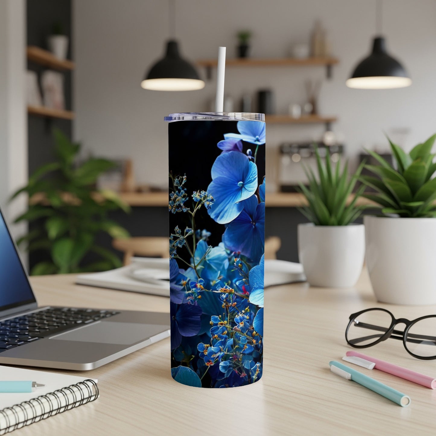 Blue floral pattern on a black tumbler with straw on a desk.