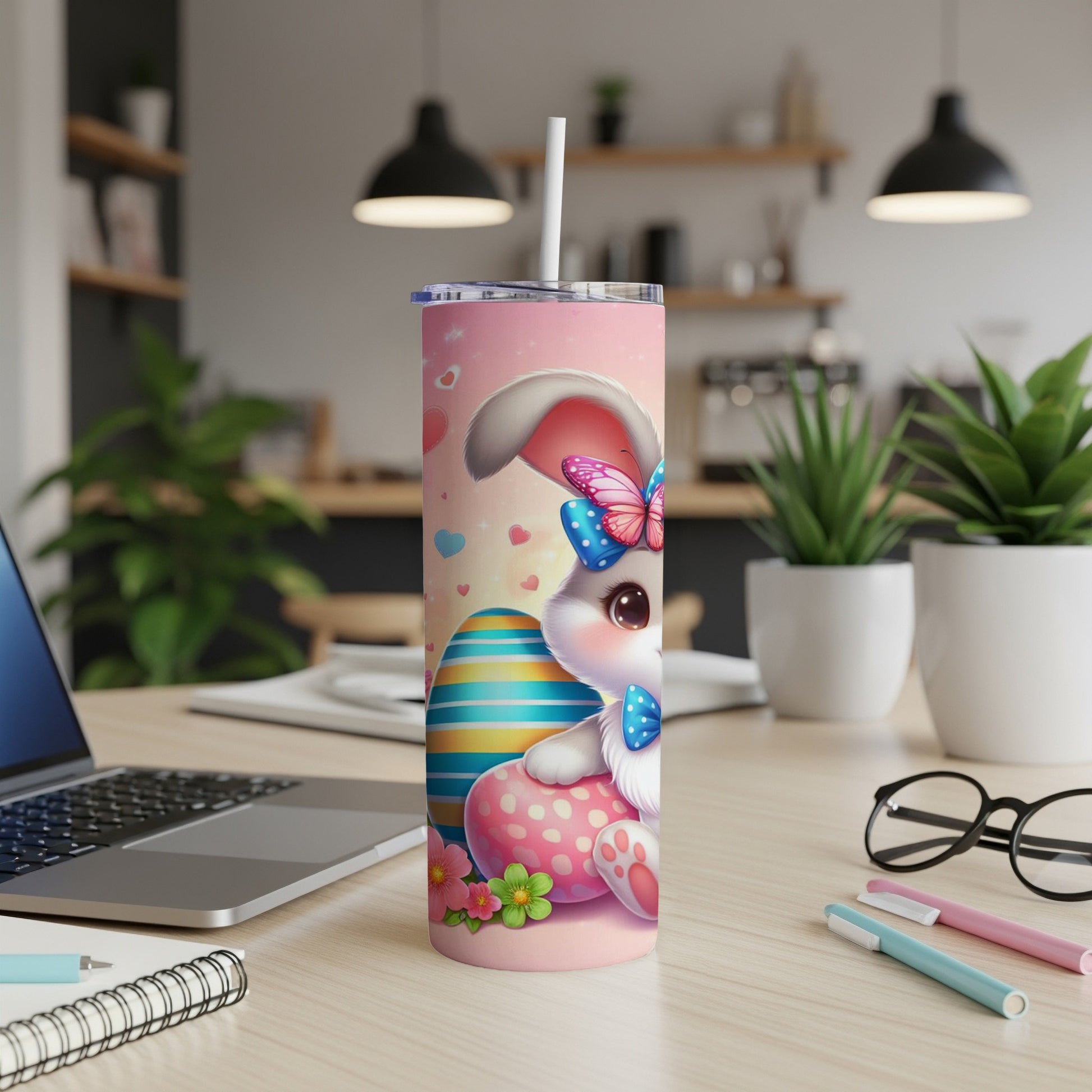 Pink tumbler with a cartoon bunny and Easter egg design, on a desk.