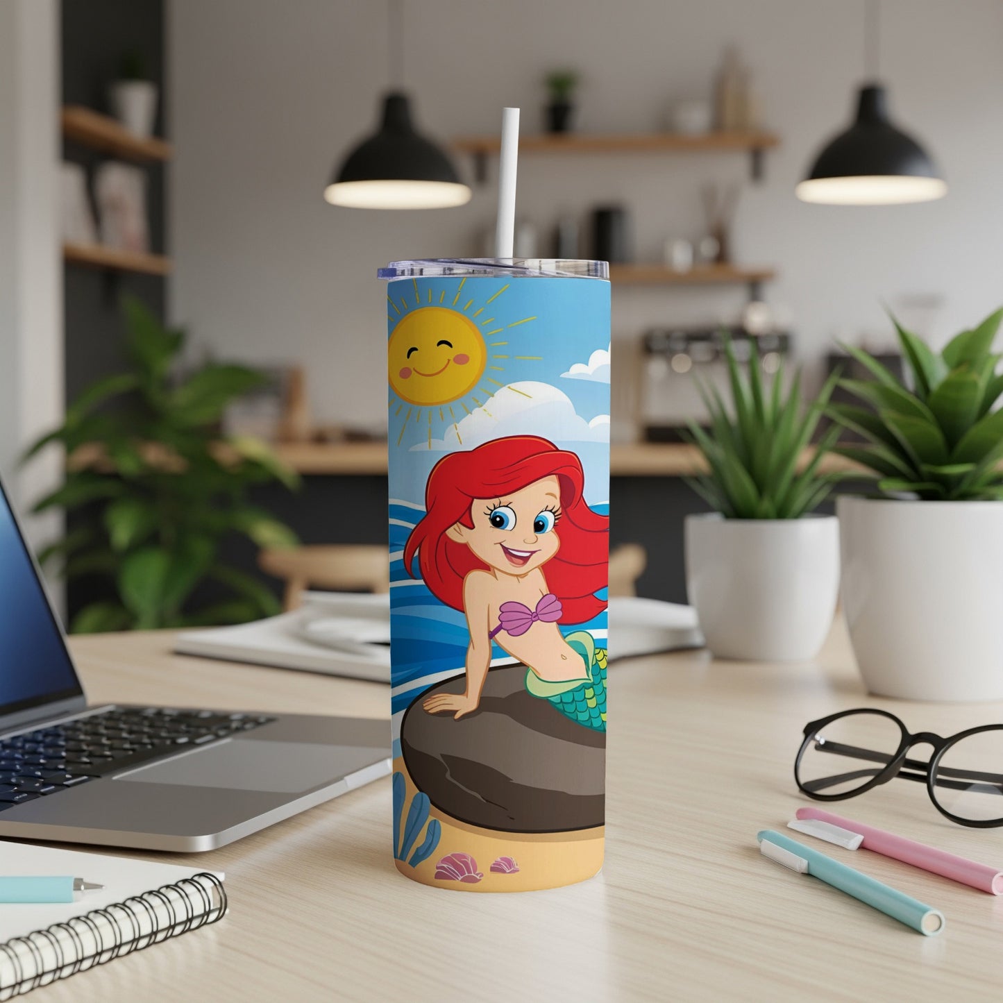 Ariel the mermaid sits on a rock under a smiling sun, holding a straw.