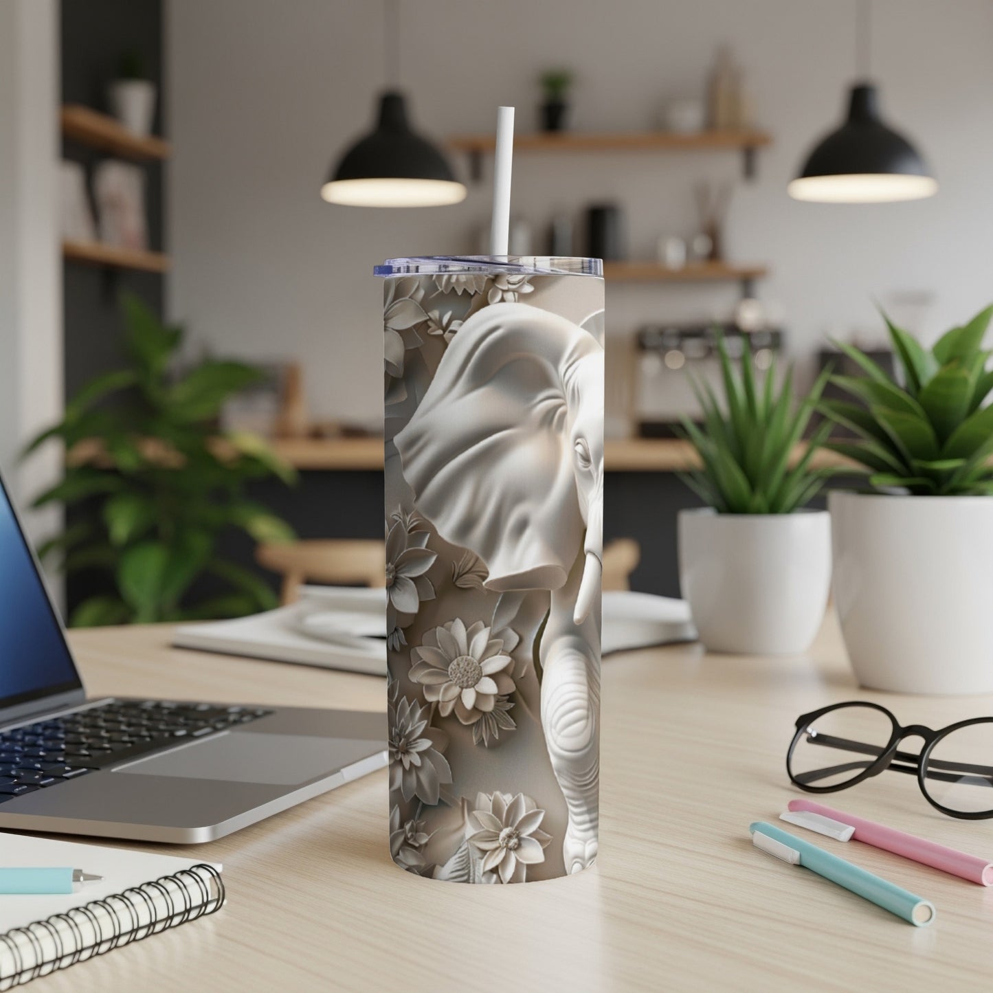 Embossed elephant design on a white tumbler with straw, placed on a desk.