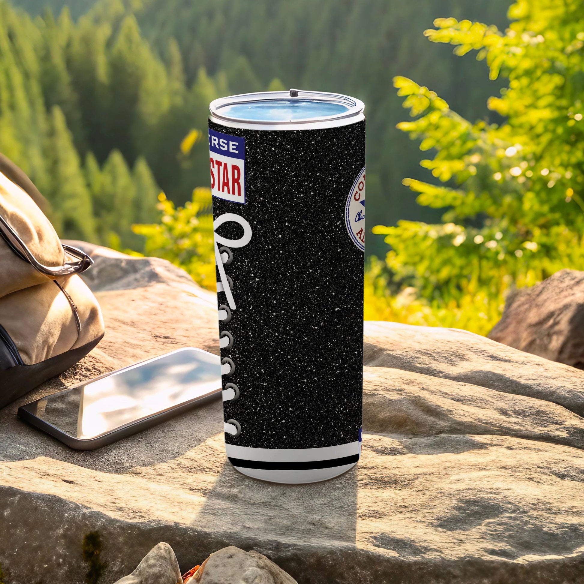 Black Converse star logo tumbler with white laces on a rock with a backpack and phone.