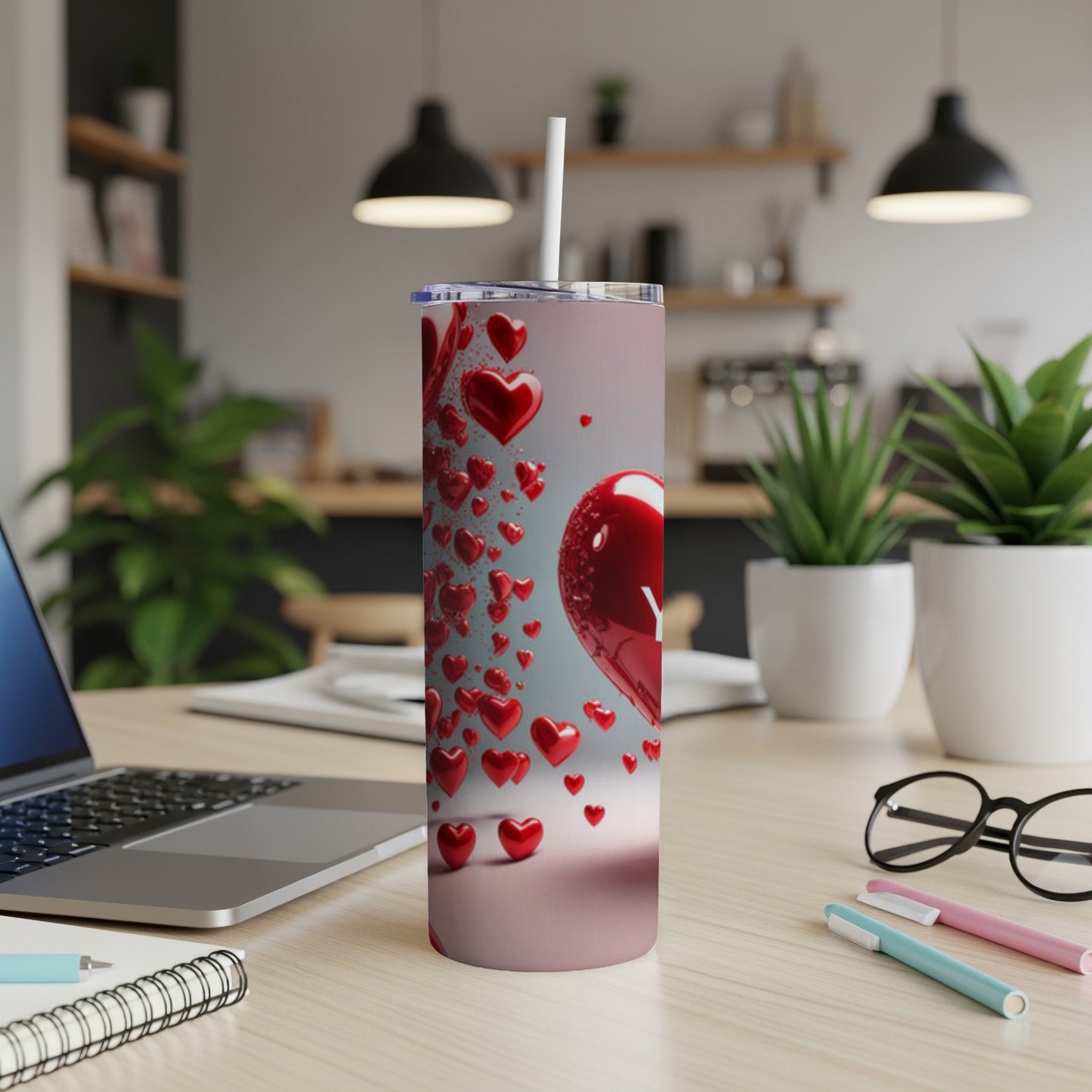 Tall tumbler with red hearts, white straw, on a desk.