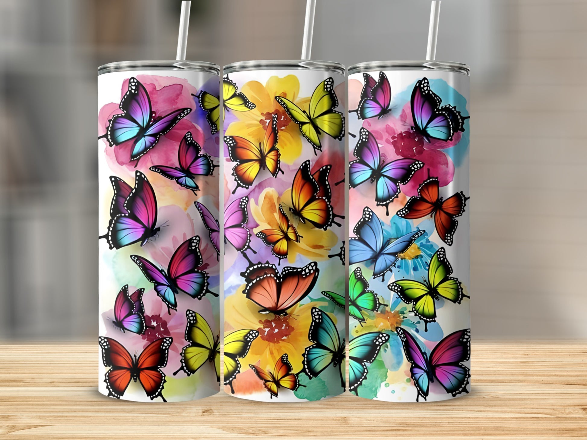 Three tumblers with colorful butterfly designs displayed on a wooden surface.