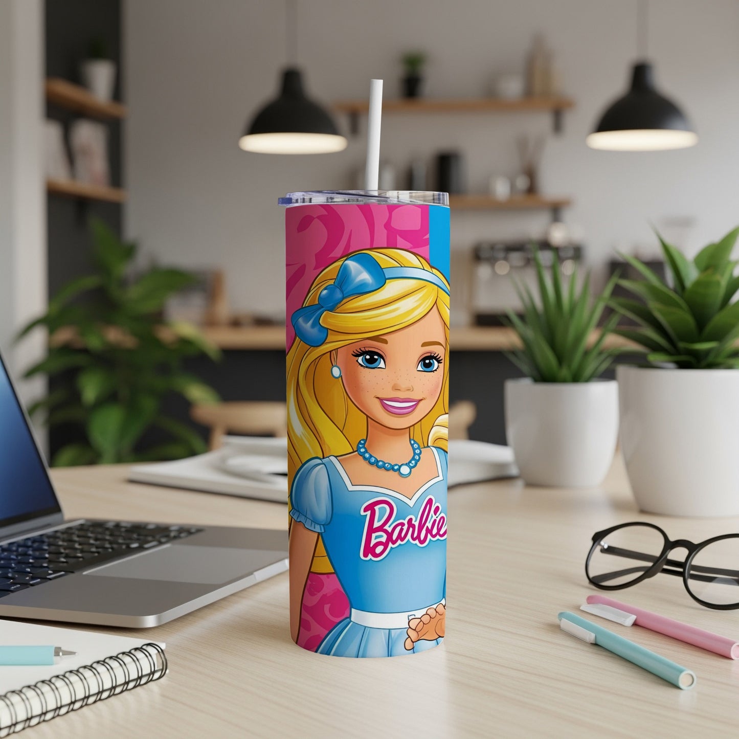 Barbie illustration on a pink and blue tumbler with a straw, on a desk.