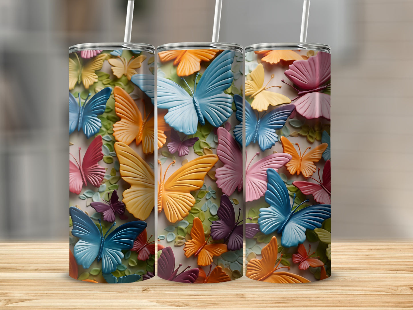 Three colorful butterfly pattern tumblers with straws on a wooden surface.