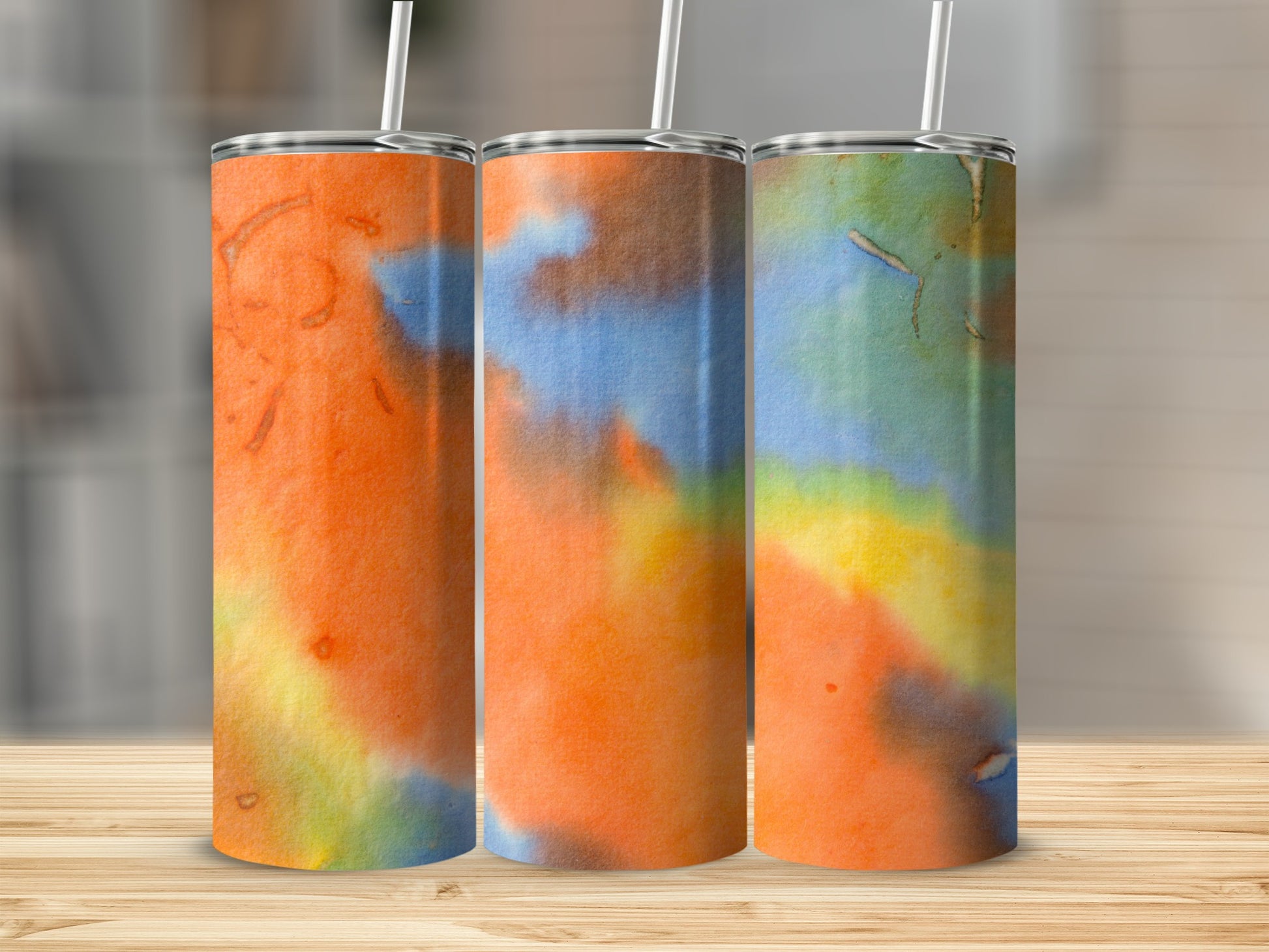 Three tumblers with watercolor designs in orange, blue, yellow, and green.