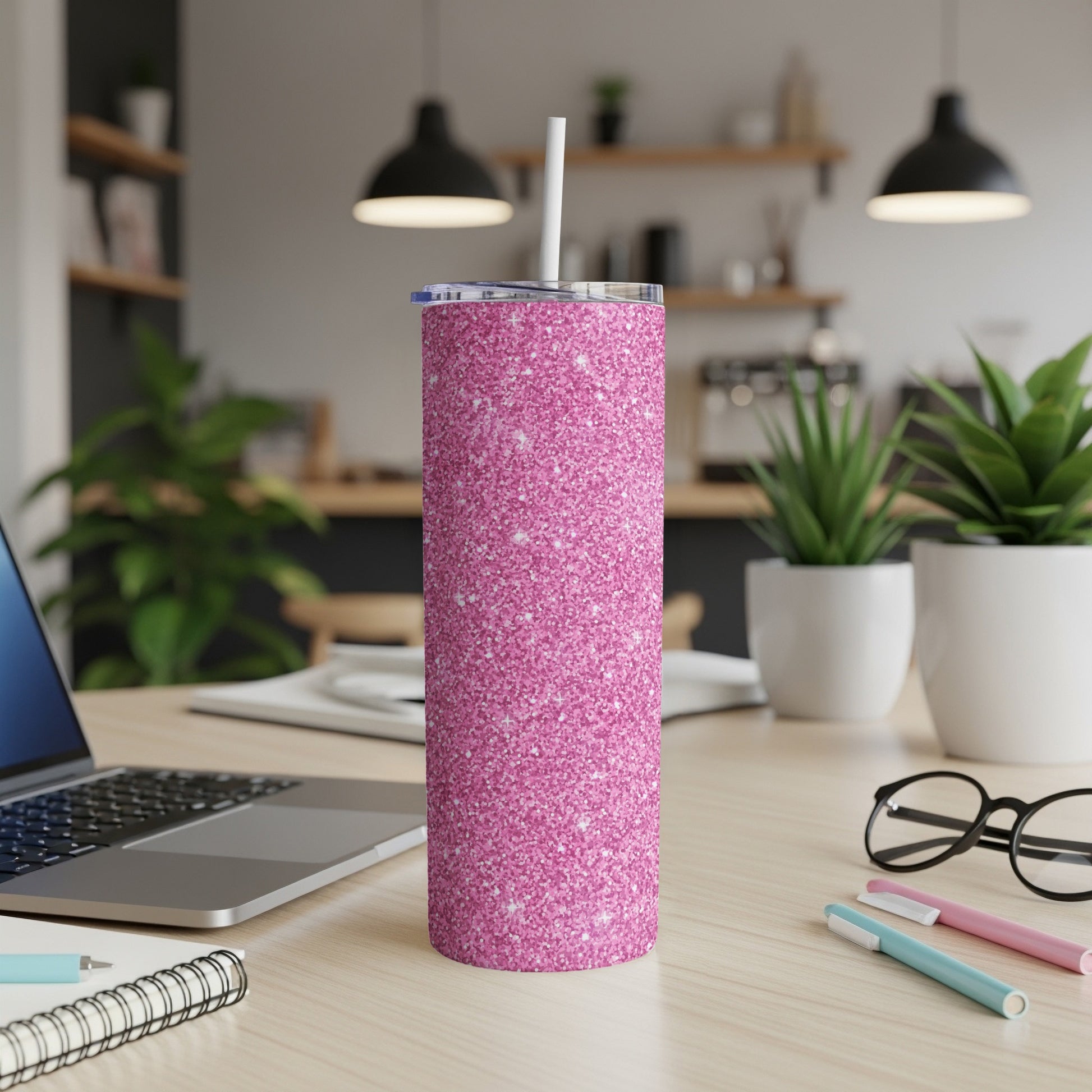 Pink glitter tumbler with straw on a desk with a laptop and pens.