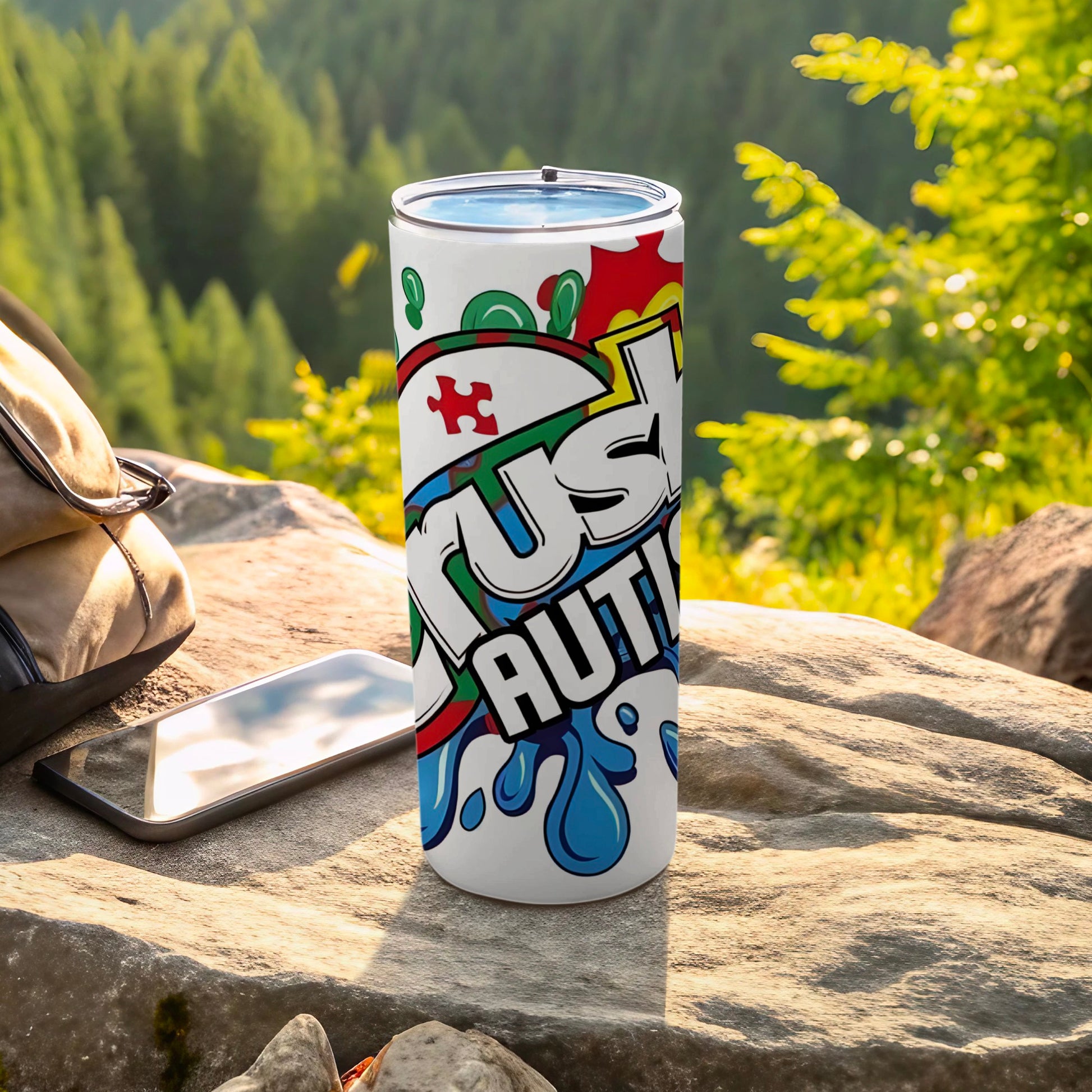 White tumbler with "Just Autism" text and puzzle pieces, beside a phone and backpack.