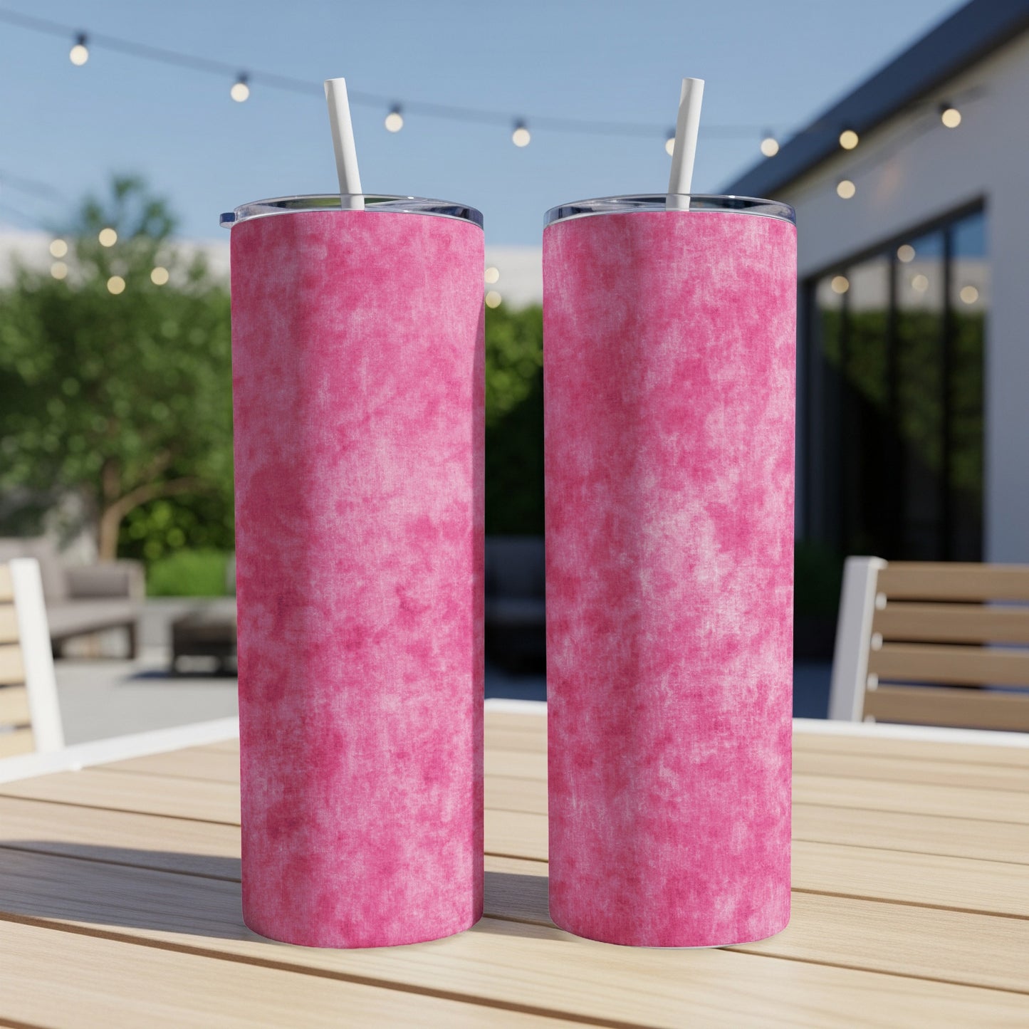 Two pink marbled tumblers with white straws sit on a wooden table.
