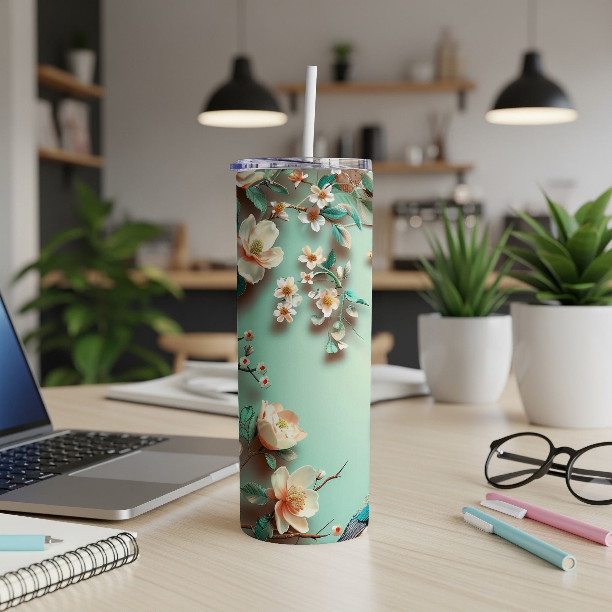 Tall tumbler with floral design and straw on a desk with a laptop.