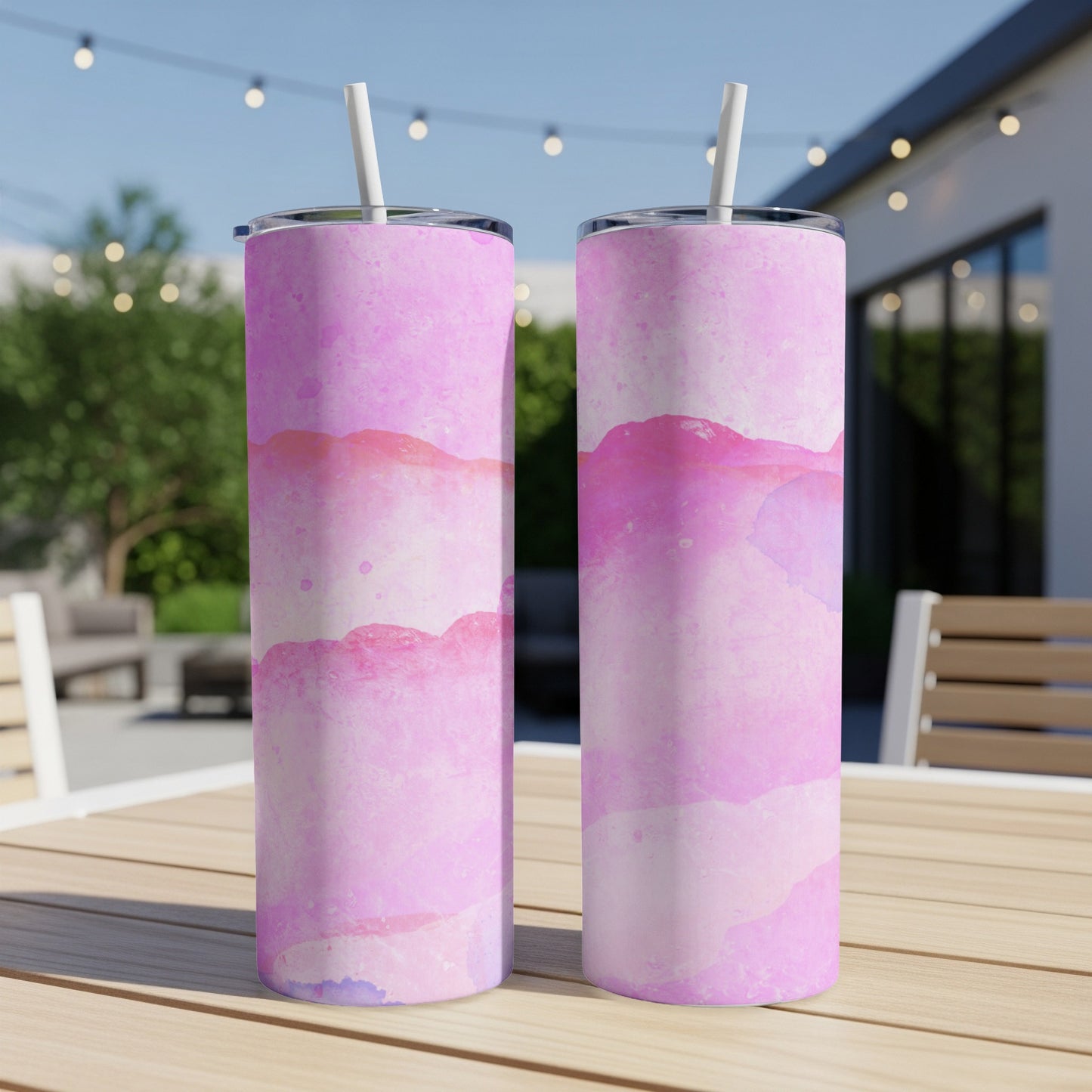 Two pink watercolor print tumblers with straws sit on a wooden table.