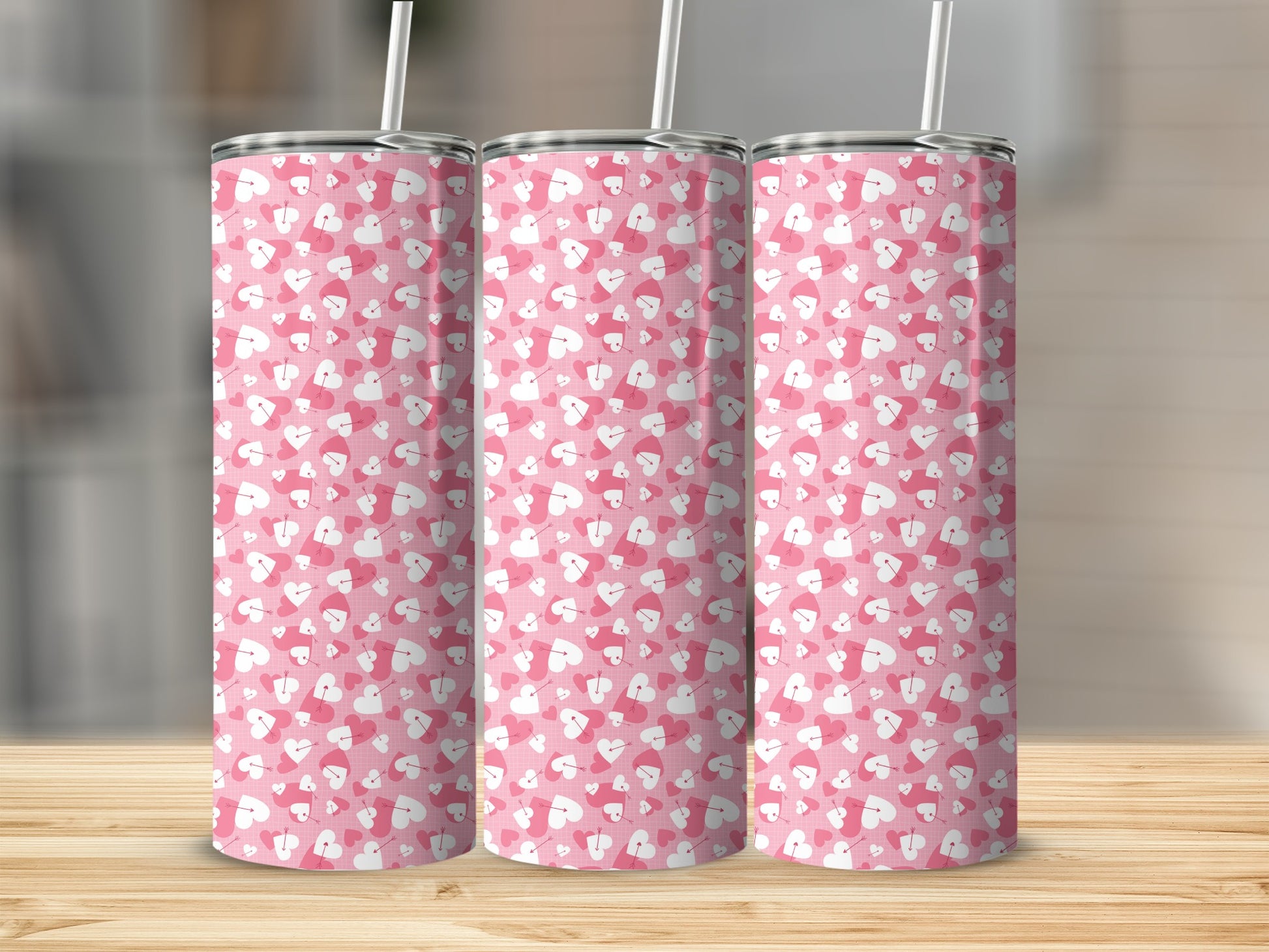Pink tumblers with a white and pink heart pattern and straws on a wooden surface.