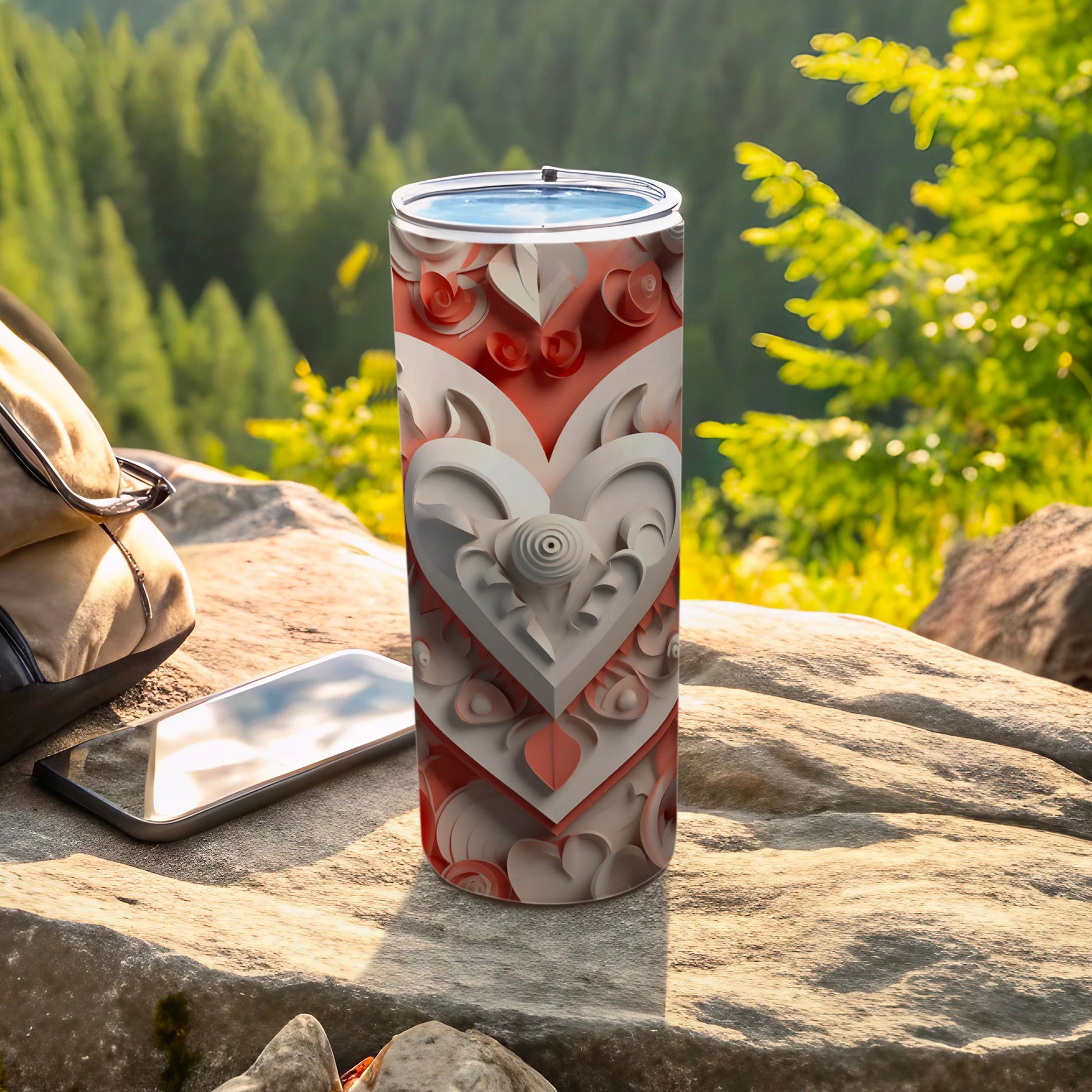 White and red layered heart pattern tumbler on rock with phone and backpack.