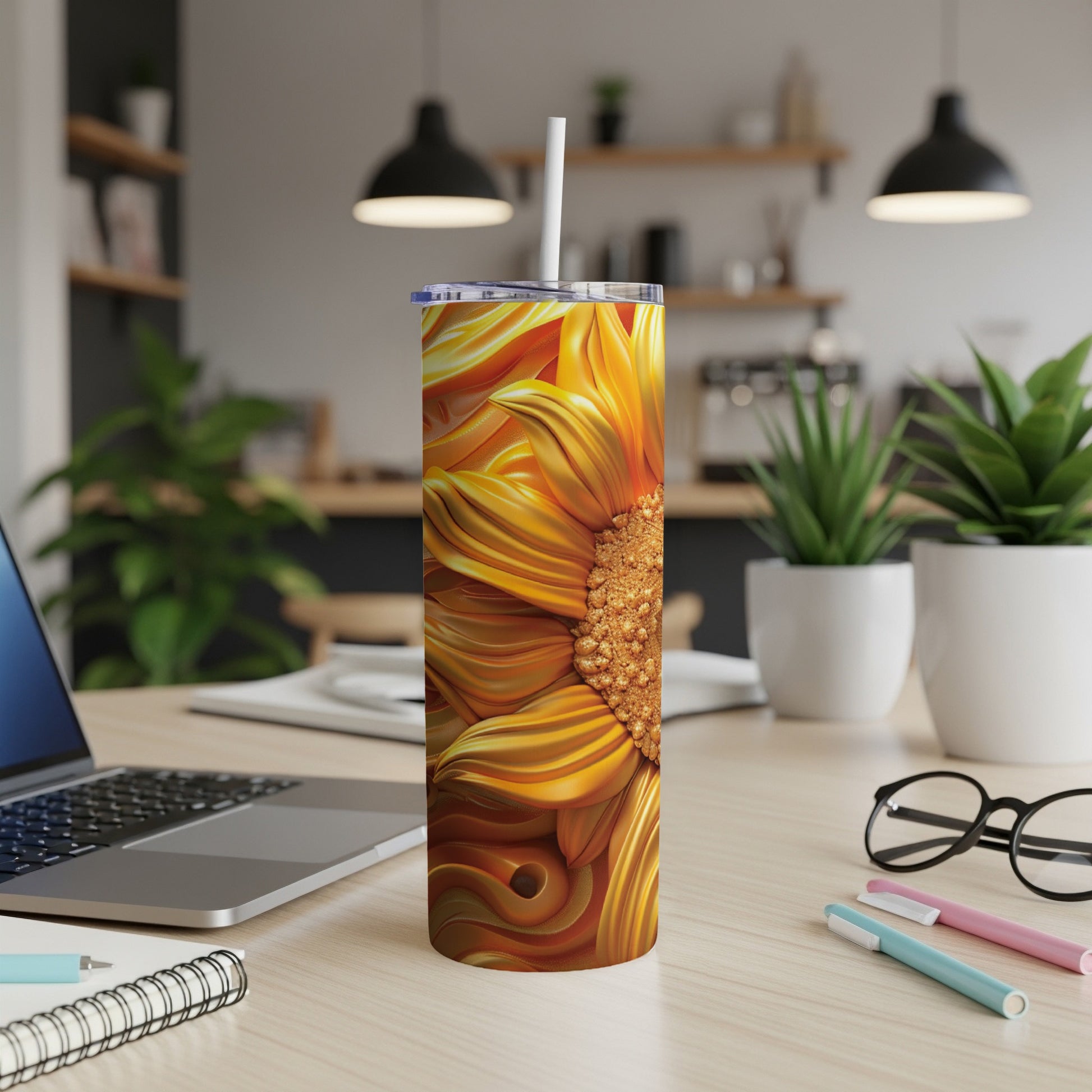 Sunflower tumbler with straw on a desk with laptop and pens.