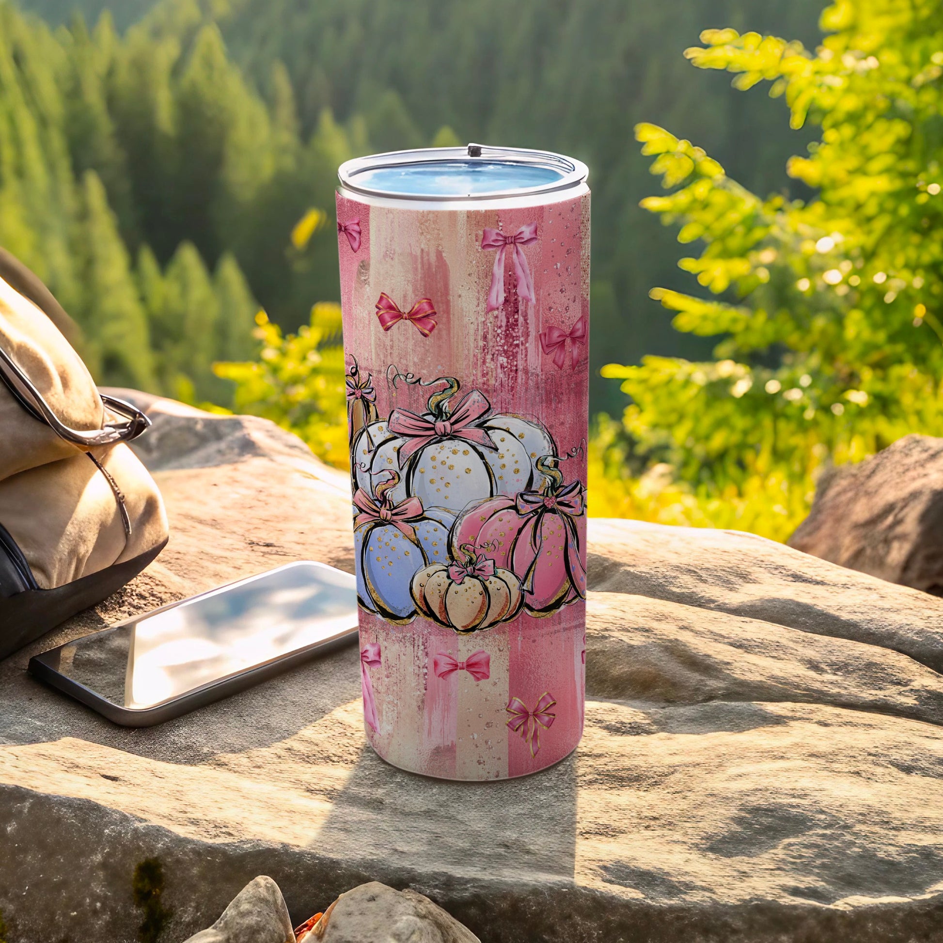 Pink plaid tumbler with pastel pumpkins and bows, on rocks with phone.