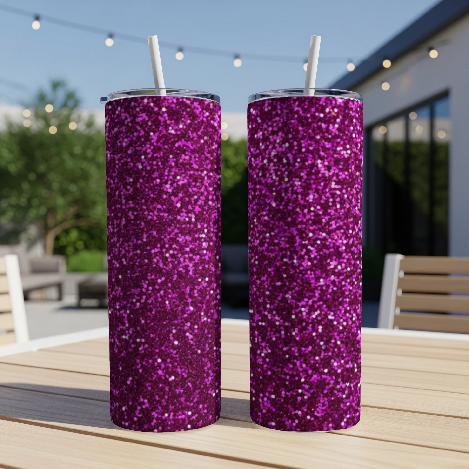 Two magenta glitter tumblers with straws on a wooden table outdoors.