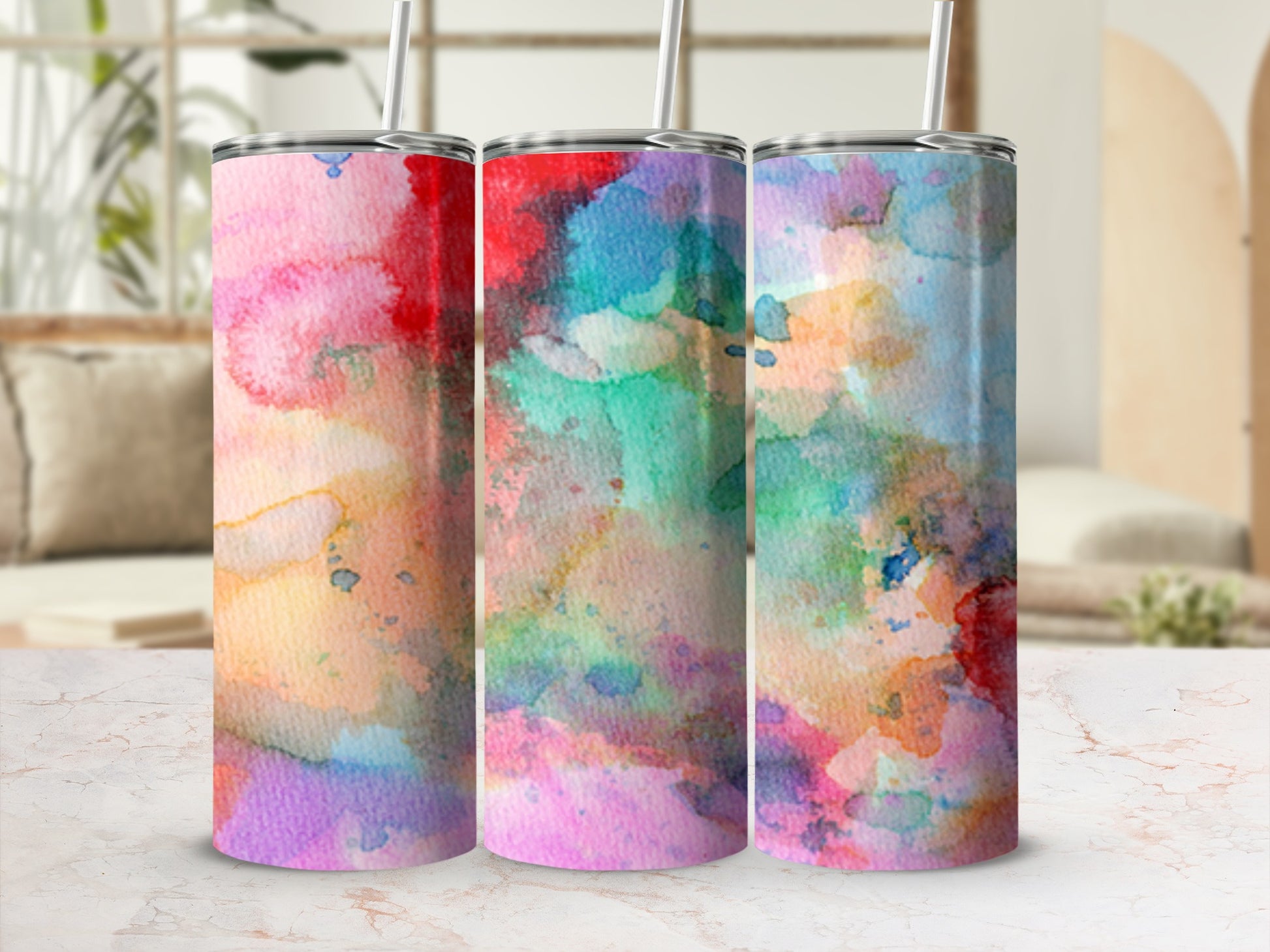 Three tumblers with colorful watercolor designs on a marble surface.