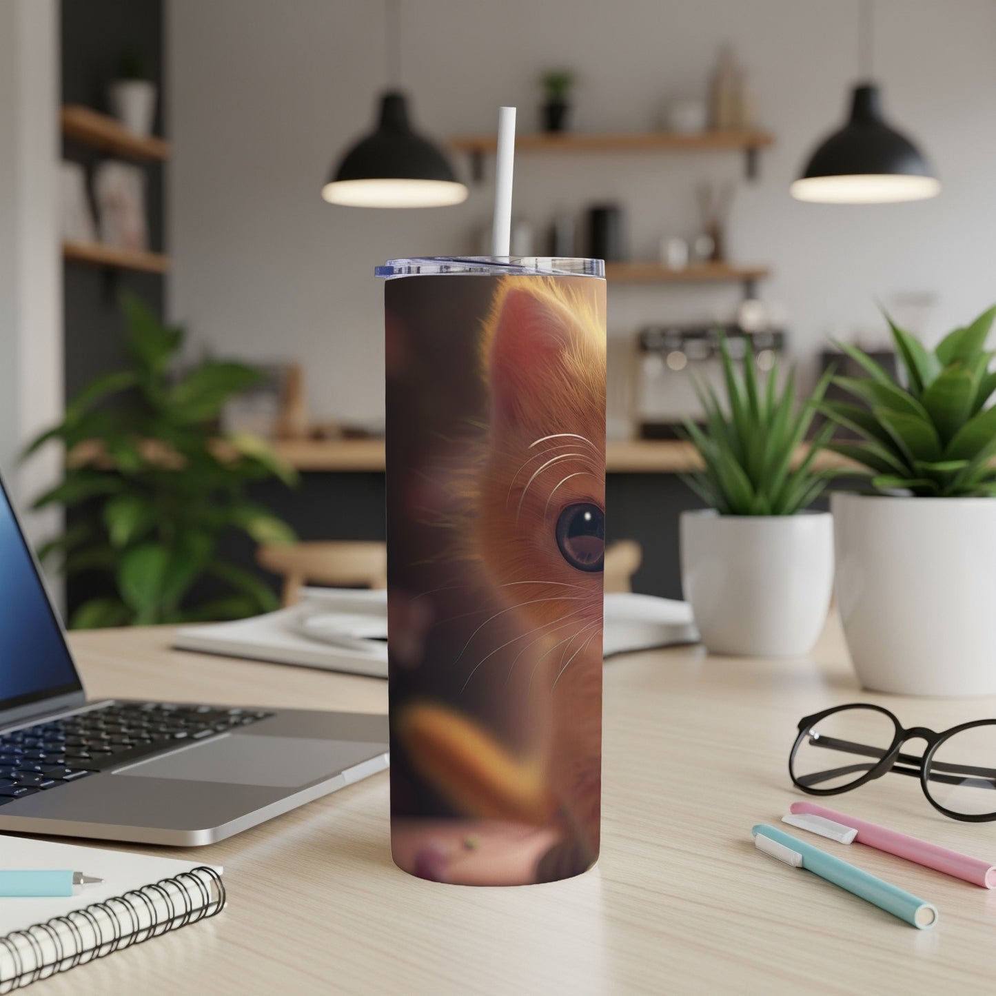 Close-up of a cat's face on a tumbler, with a laptop and office supplies.