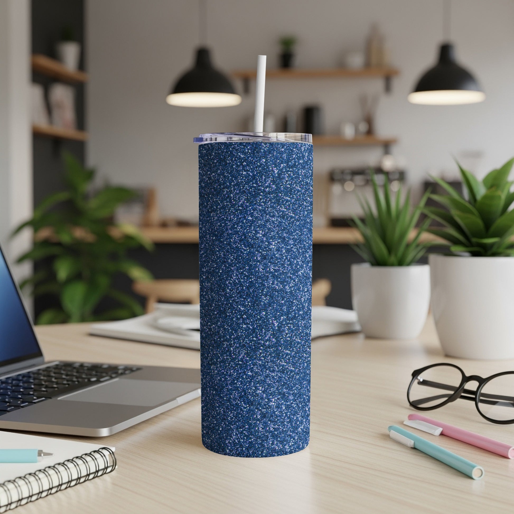 Sparkly navy blue tumbler with a straw on a wooden desk.