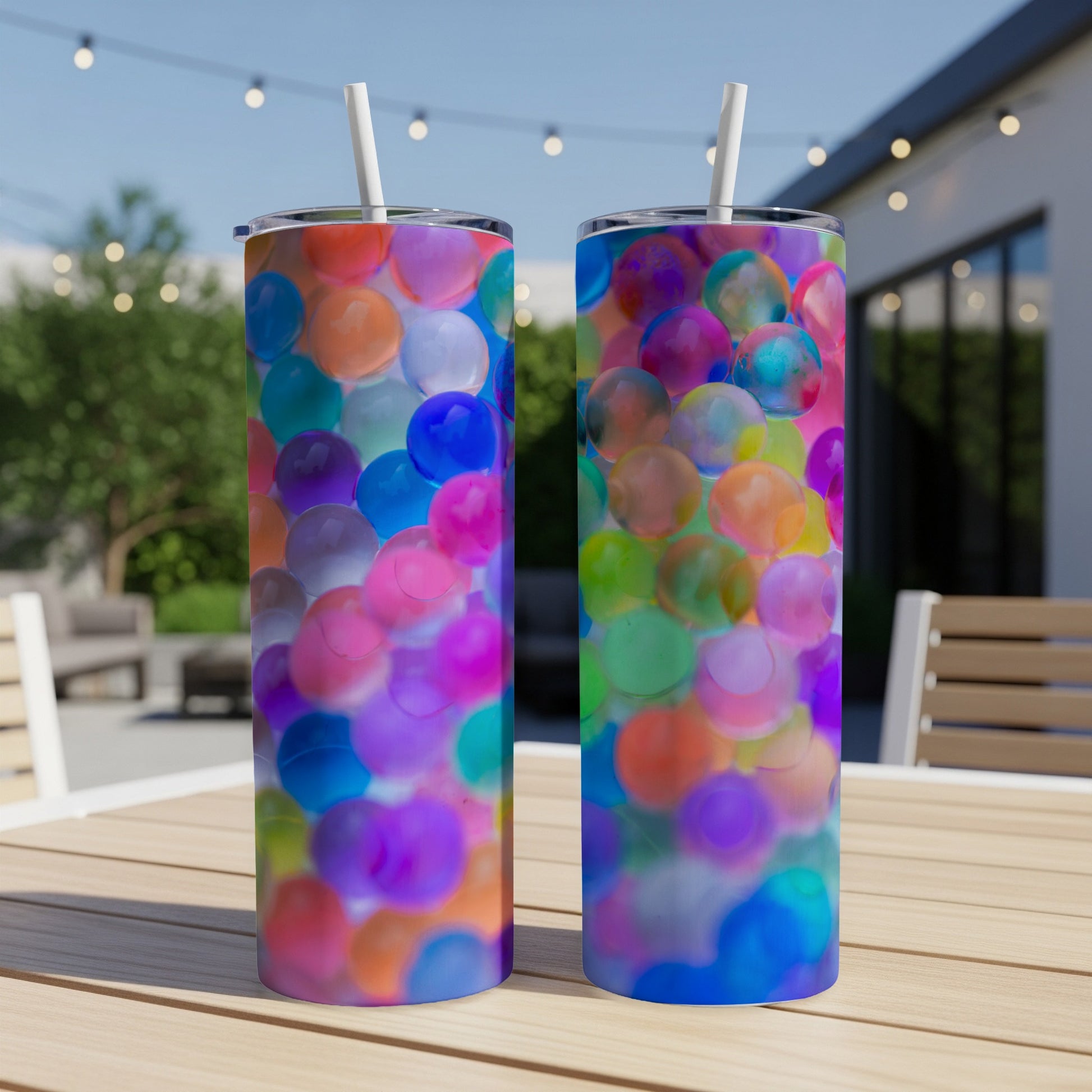 Two colorful orb-filled tumblers on a wooden table outdoors.