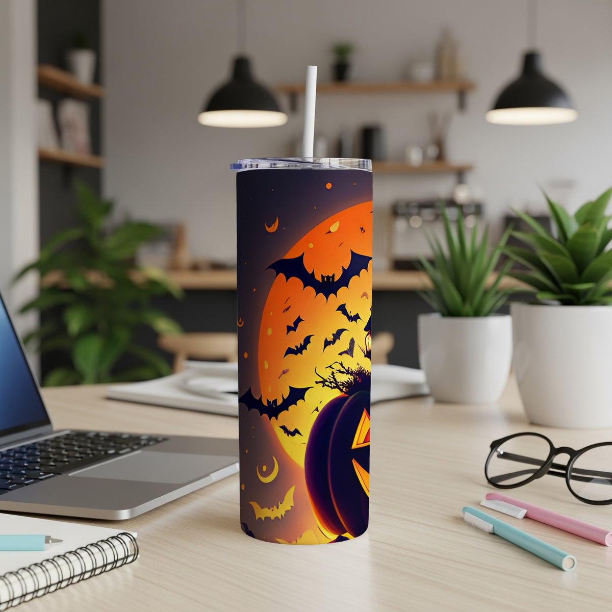 Halloween tumbler with pumpkin, bats, and moon on a desk with laptop and plants.