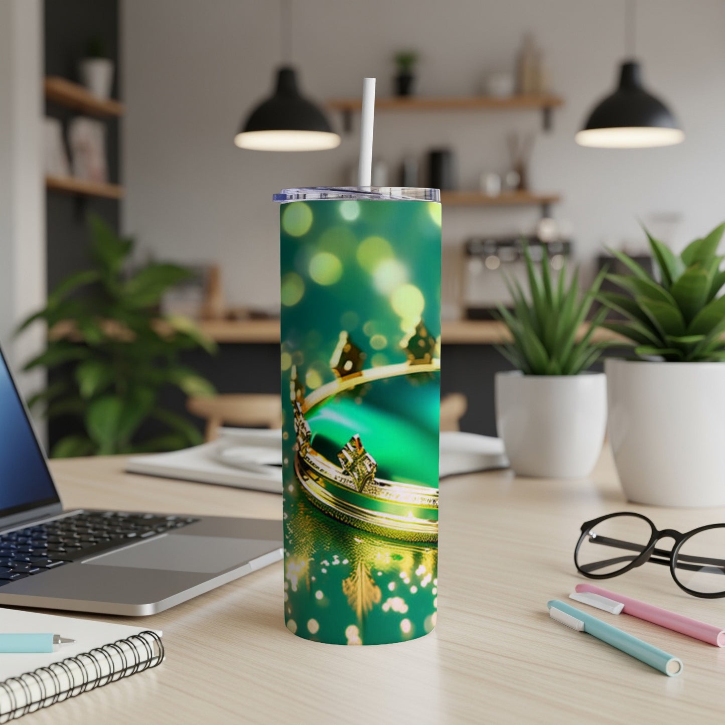 Green tumbler with gold crown and bokeh effect on desk.