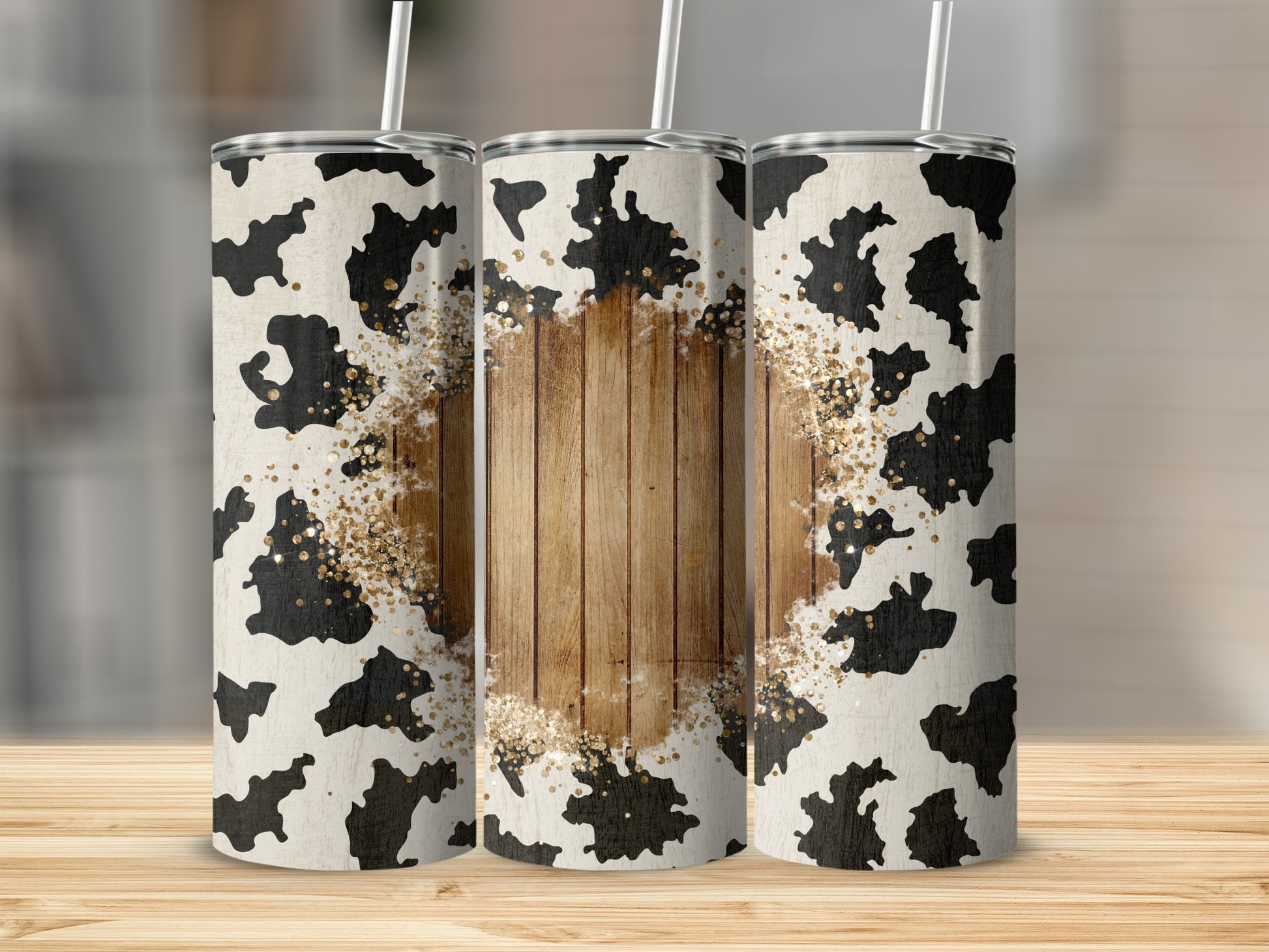 Three tumblers with cow print and wood grain design, accented with gold glitter.