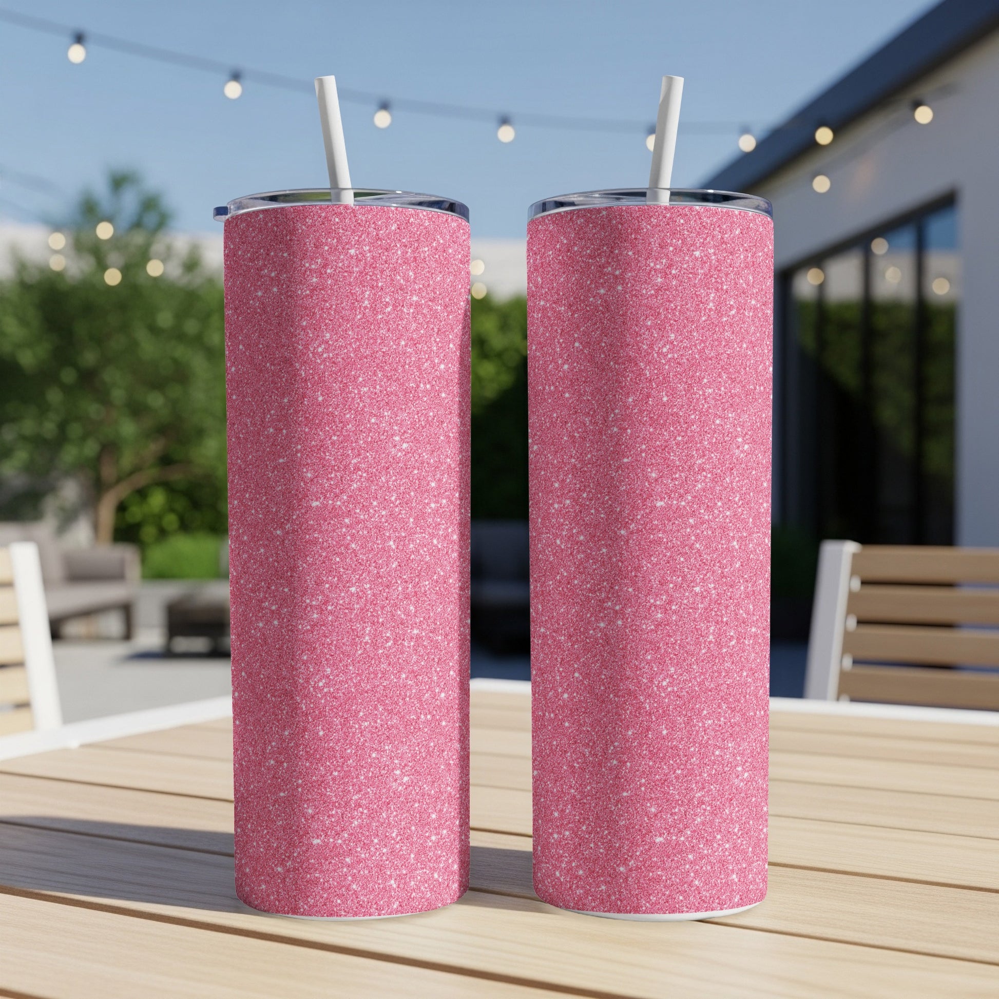 Two pink glitter tumblers with white straws sit on a wooden table.