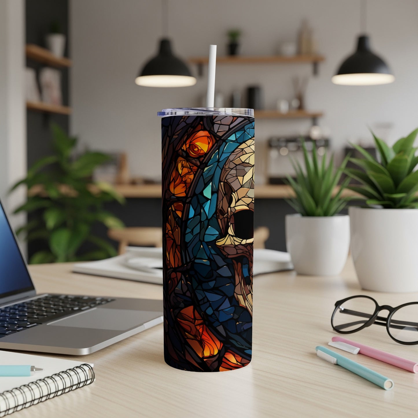 Stained glass skull tumbler with a straw on a desk.