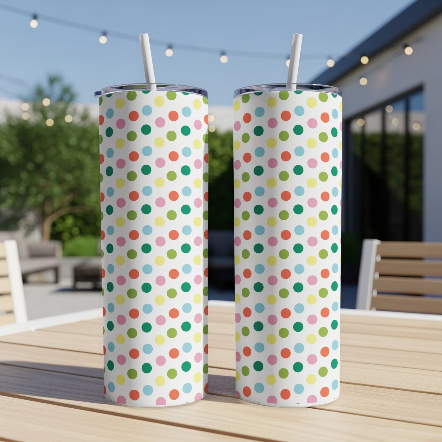Two tall tumblers with colorful polka dots on a wooden table outdoors.