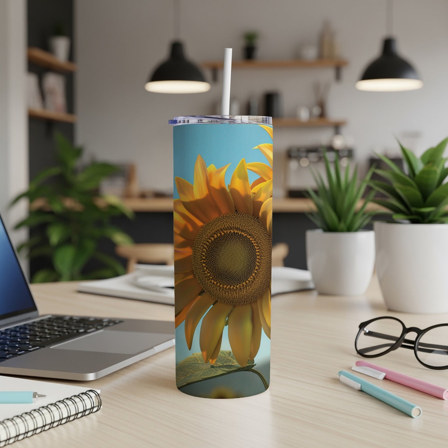 Tall tumbler with sunflower image on desk next to laptop and pens.