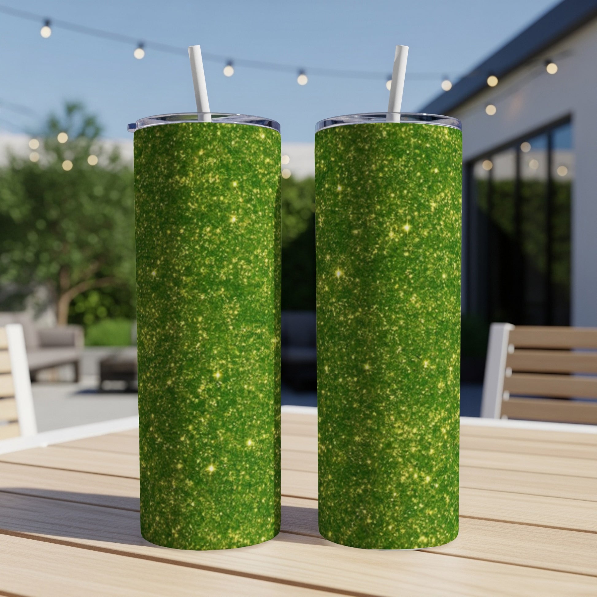 Two green glitter tumblers with straws on a wooden table outdoors.