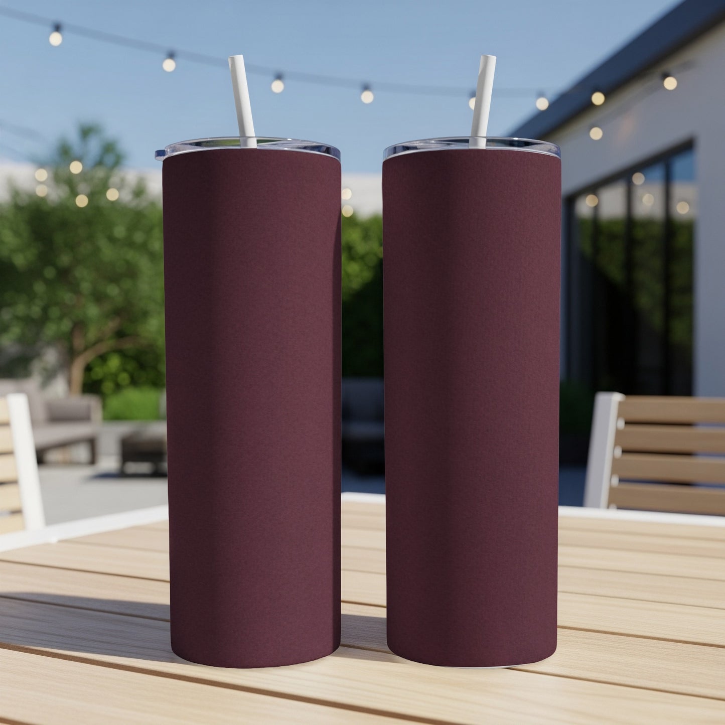 Two dark red tumblers with white straws stand on a wooden table outdoors.