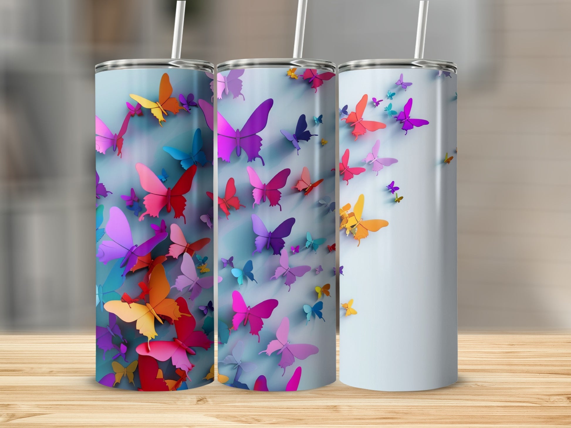 Three tumblers with colorful butterfly designs on a wooden surface.
