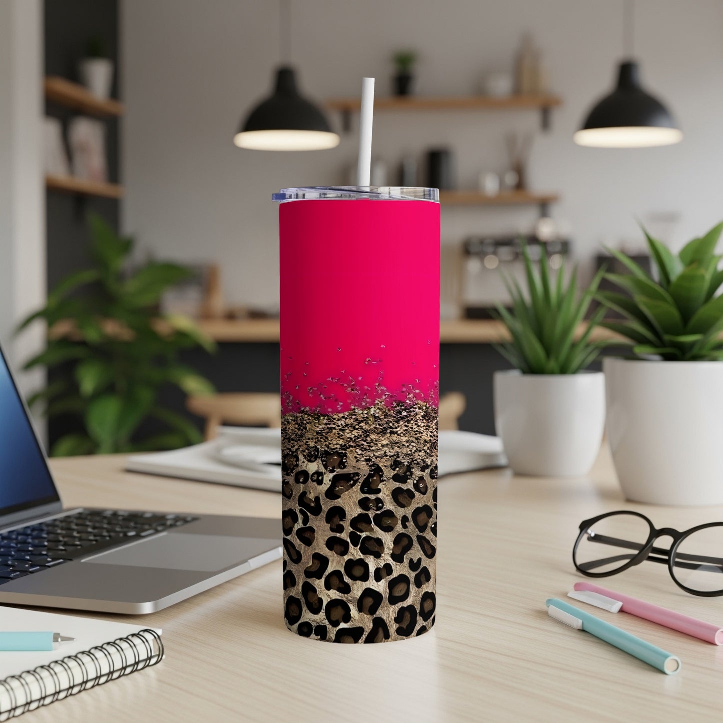 Pink and leopard print tumbler with straw on desk with laptop and pens.