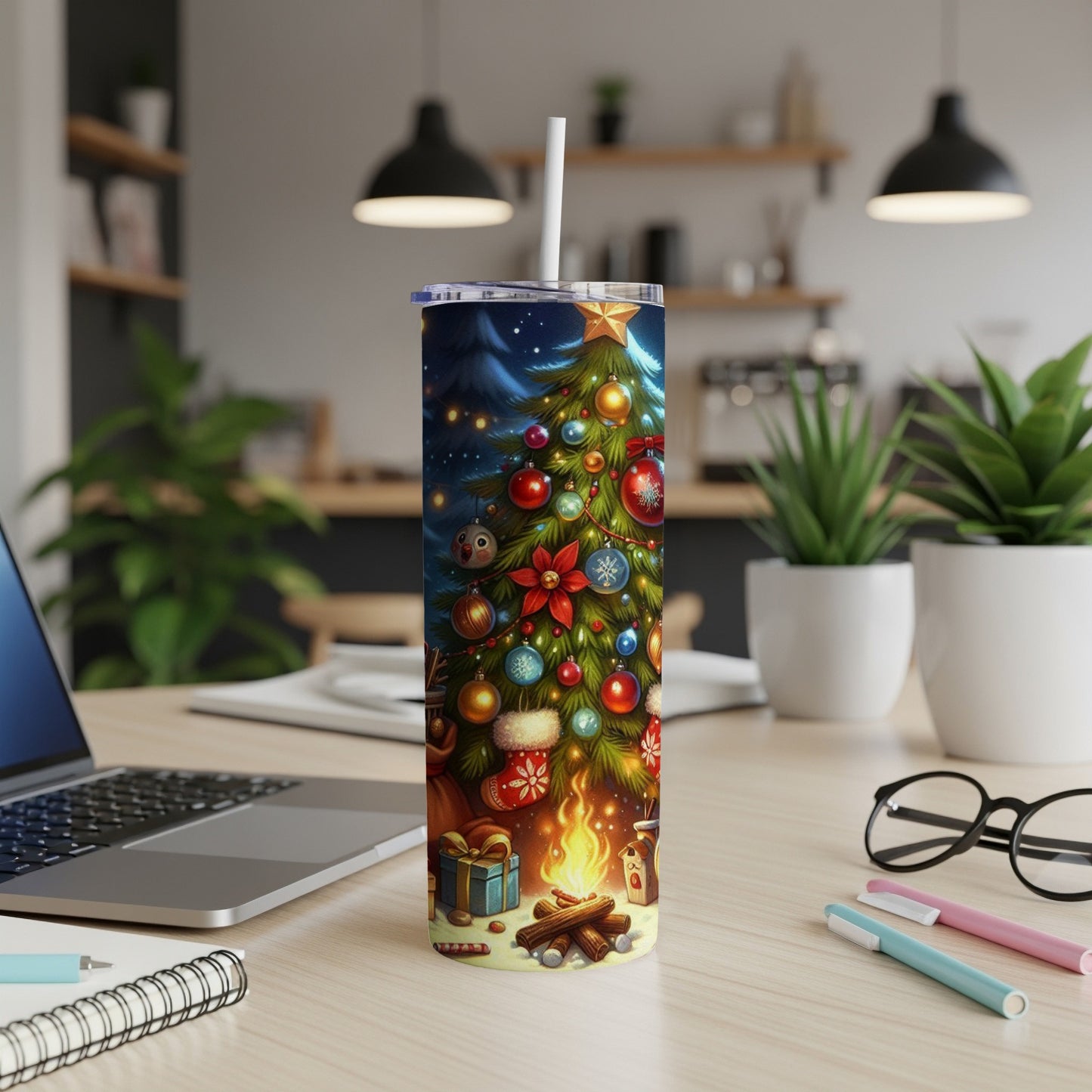 Christmas tree tumbler with ornaments and campfire design on desk.