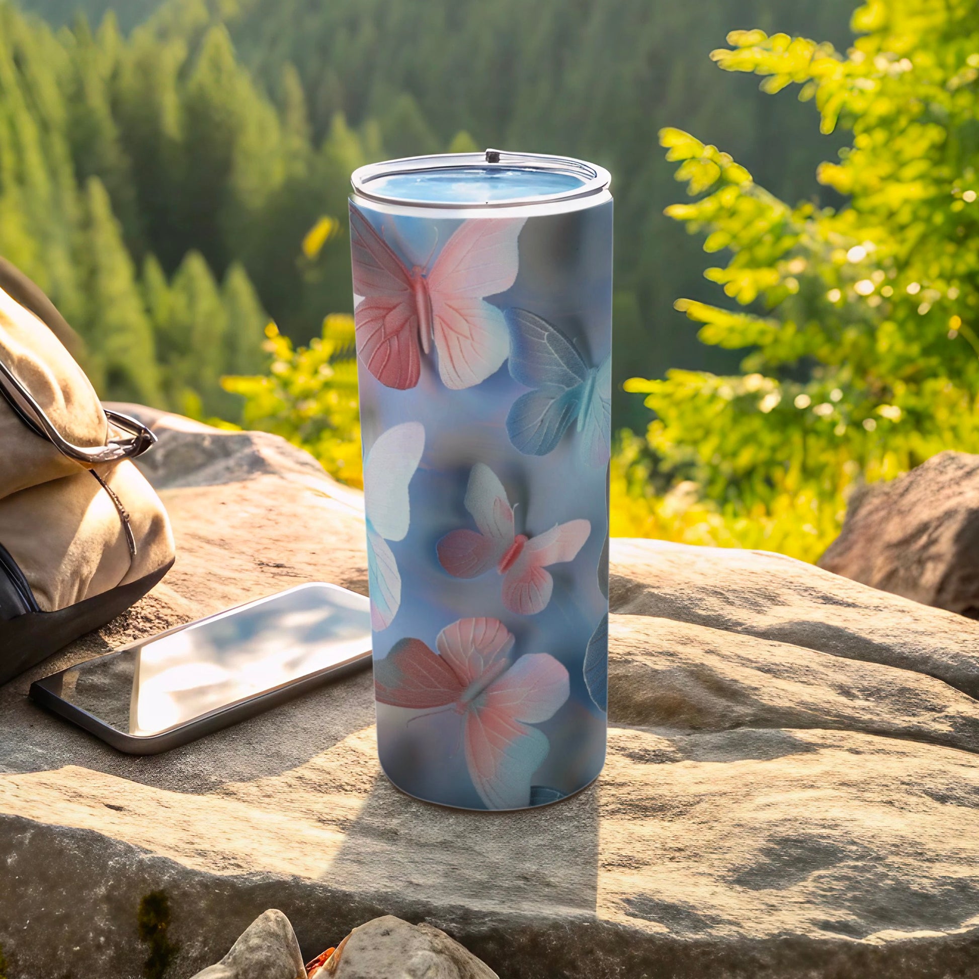 Tumbler with soft pink and blue butterflies on a rocky outdoor surface.