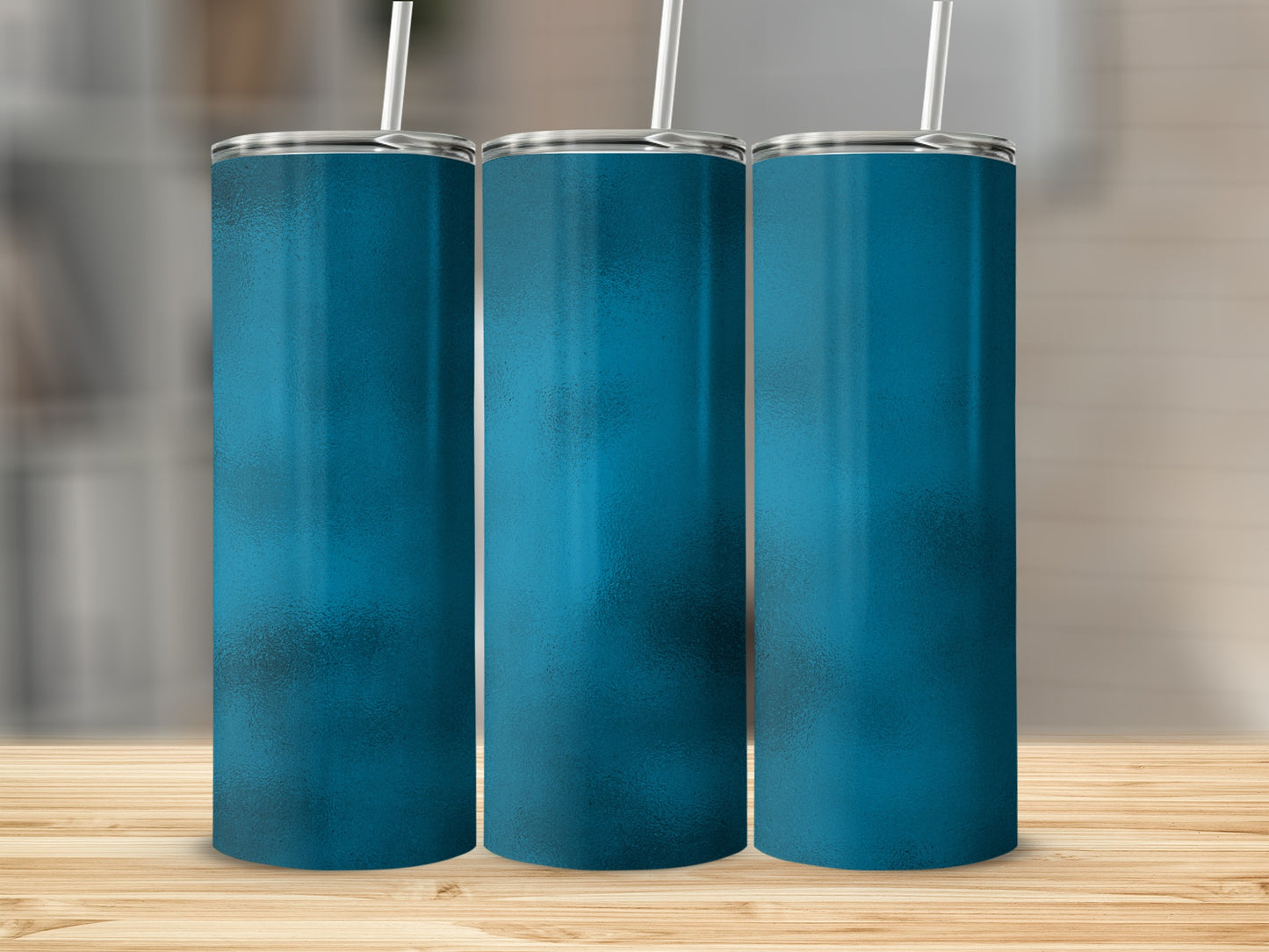 Three blue tumblers with silver lids and white straws on a wooden surface.