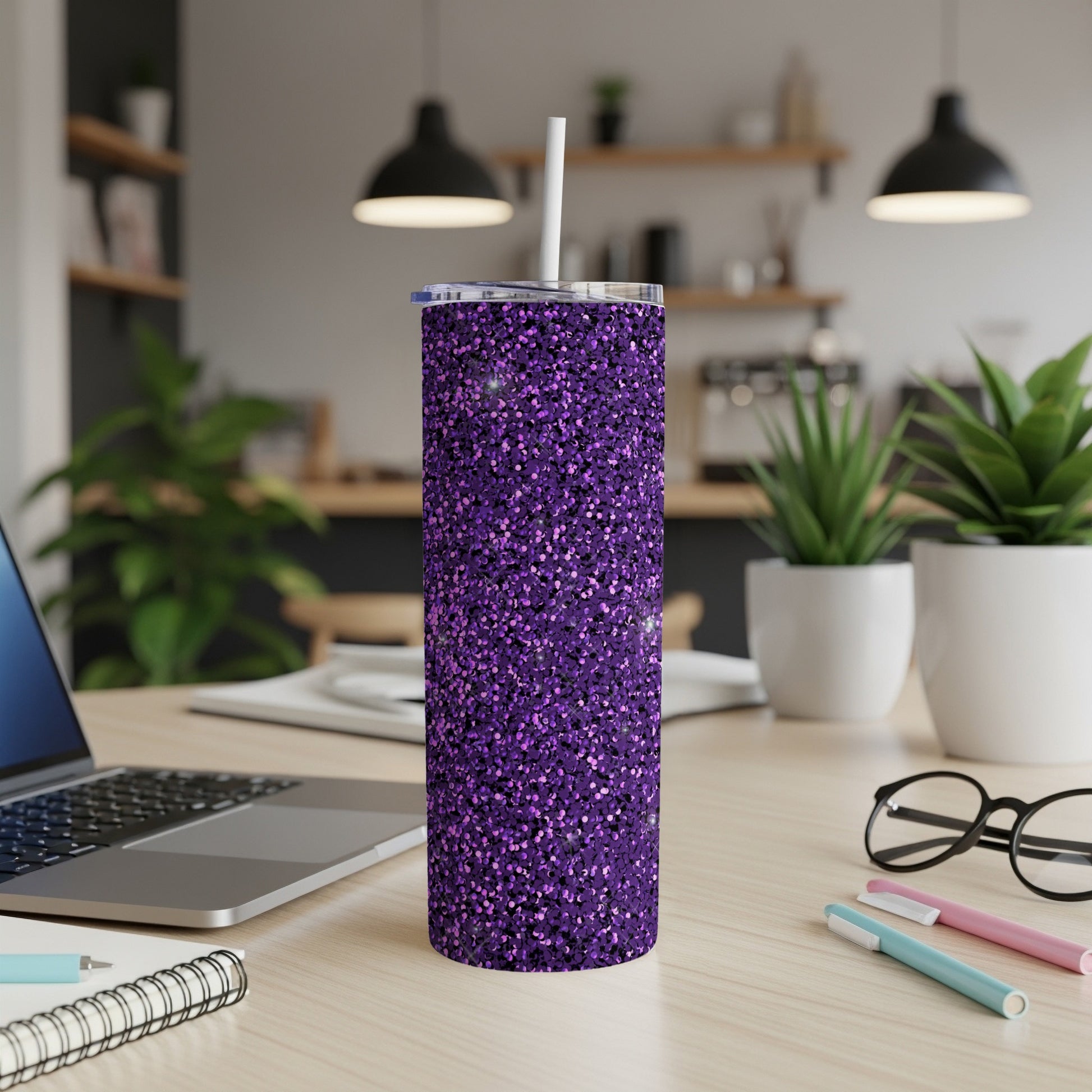 Glittery purple tumbler with white straw on a desk with laptop and pens.
