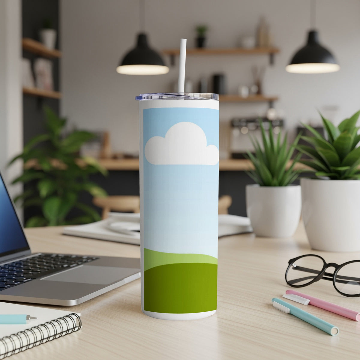 Tumbler with sky and green rolling hills design, set on a desk.