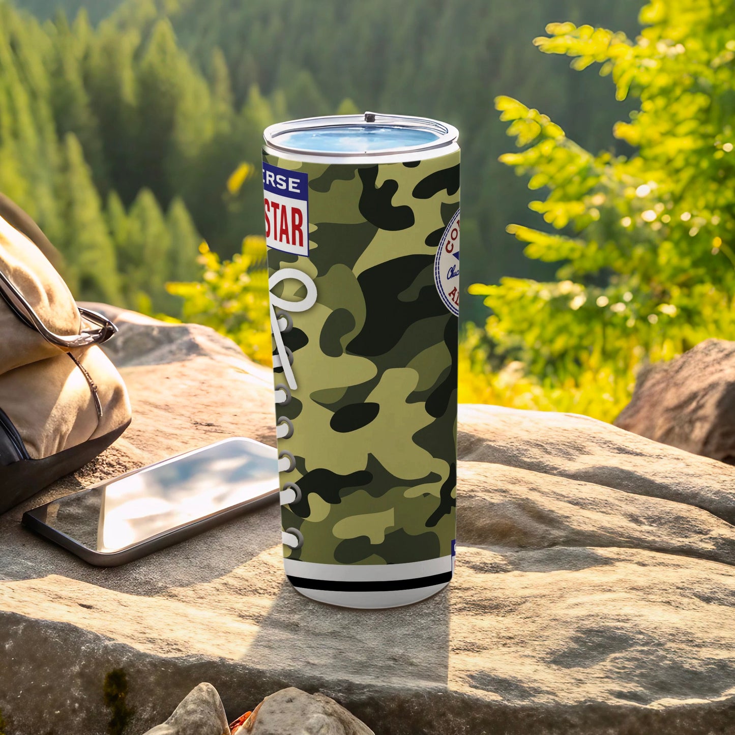 Camouflage tumbler with Converse Star logo, placed on a rock with a backpack and phone.