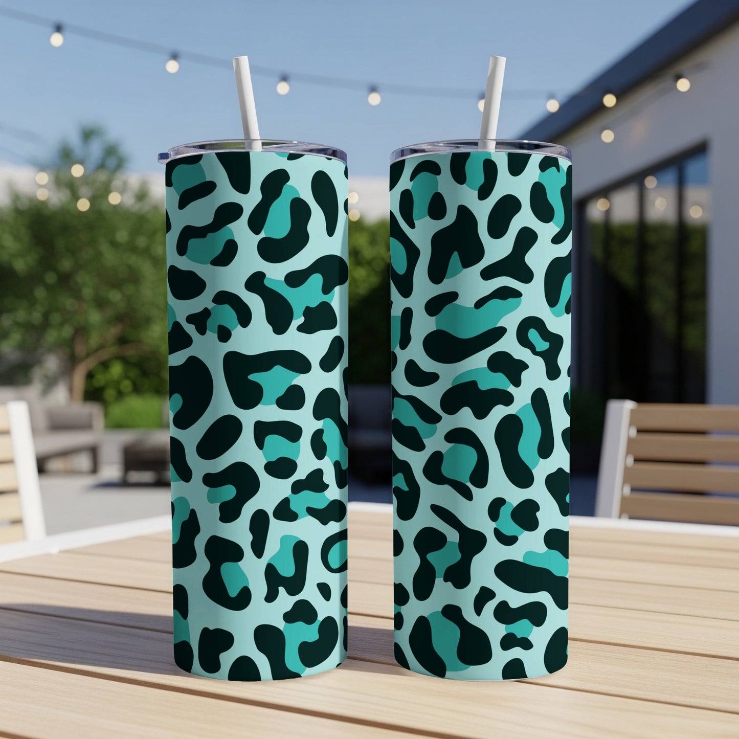 Two teal and black leopard print skinny tumblers with white straws on a wooden table.