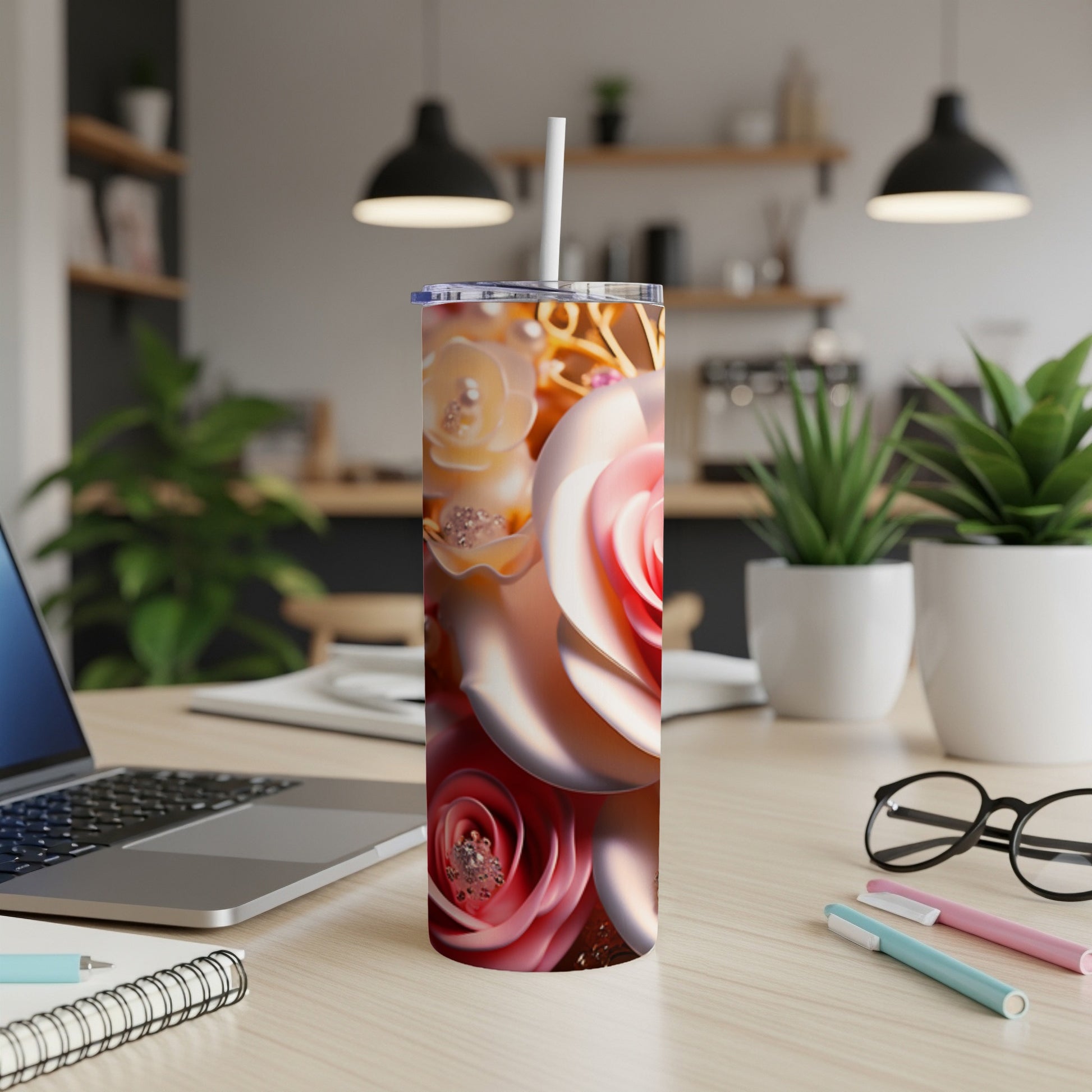 Tall tumbler with a rose floral design, laptop, and pens.